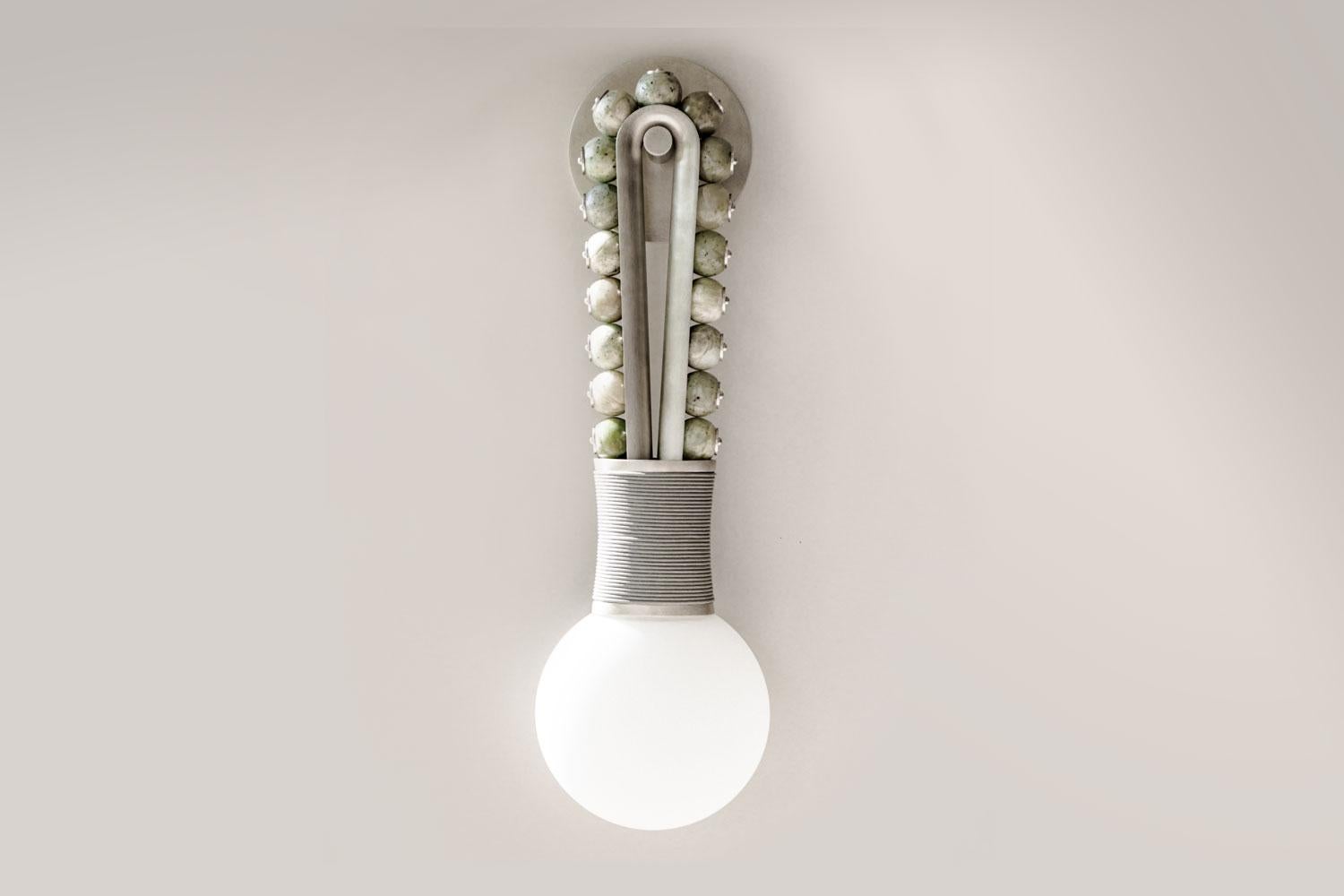 Talisman loop scone by Apparatus

Semi-precious Jade stones are pierced by finely fluted pins, affixing them to a gray leather-bound tarnished silver structure. This sconce design recalls fine details found on statues at the ancient city of