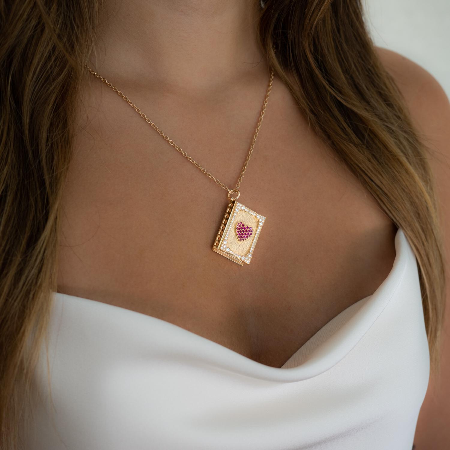 This exquisite 18K rose gold book necklace is a true work of art. The centerpiece of the necklace is a sparkling ruby heart set in a diamond frame, adding a touch of elegance and glamour. The intricate work on the spine hinges allows the book to