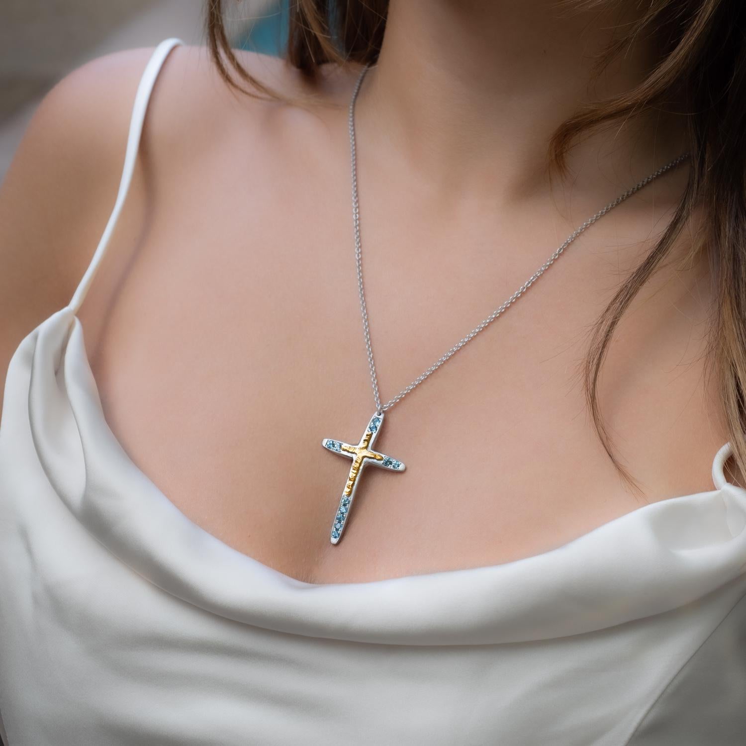 This elegant cross necklace made of 18K yellow gold and sterling silver is a beautiful combination of traditional symbolism and modern design. The cross, a timeless symbol of faith and devotion, is adorned with sparkling blue topaz, adding a touch