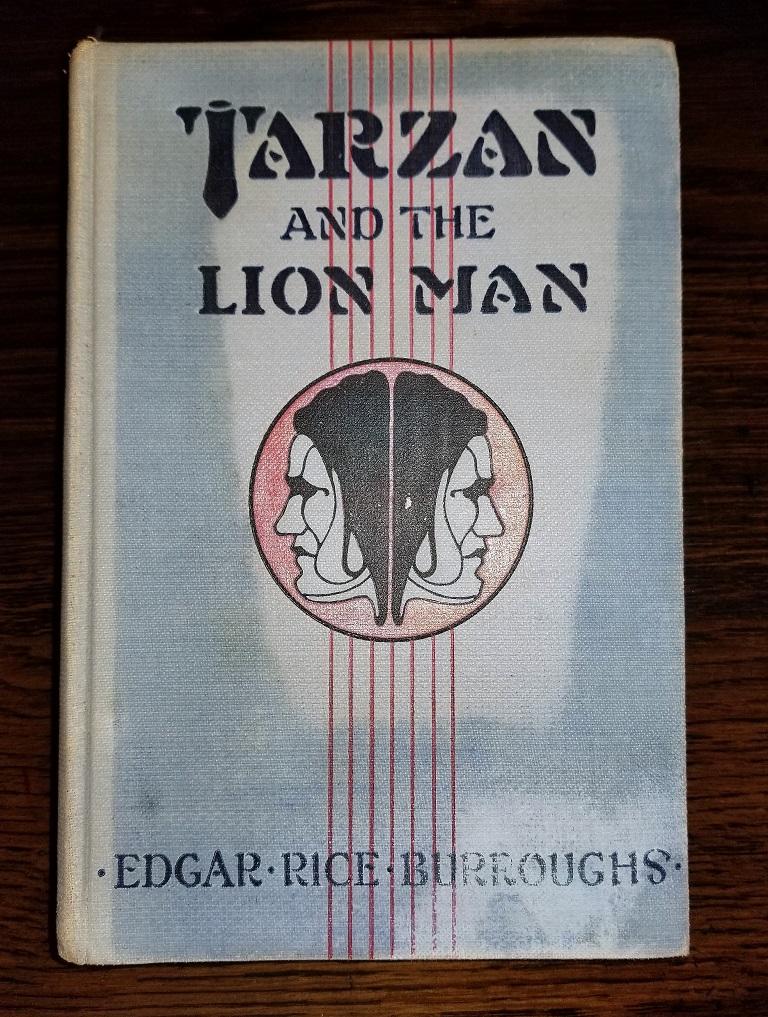 Presenting a gloriously rare book Tarzan and the Lion Man by Edgar Rice Burroughs 1st Edition.

An attractive first edition/first printing, gray decorated cloth with black lettering a red “Janus” illustration in Near Fine condition with light