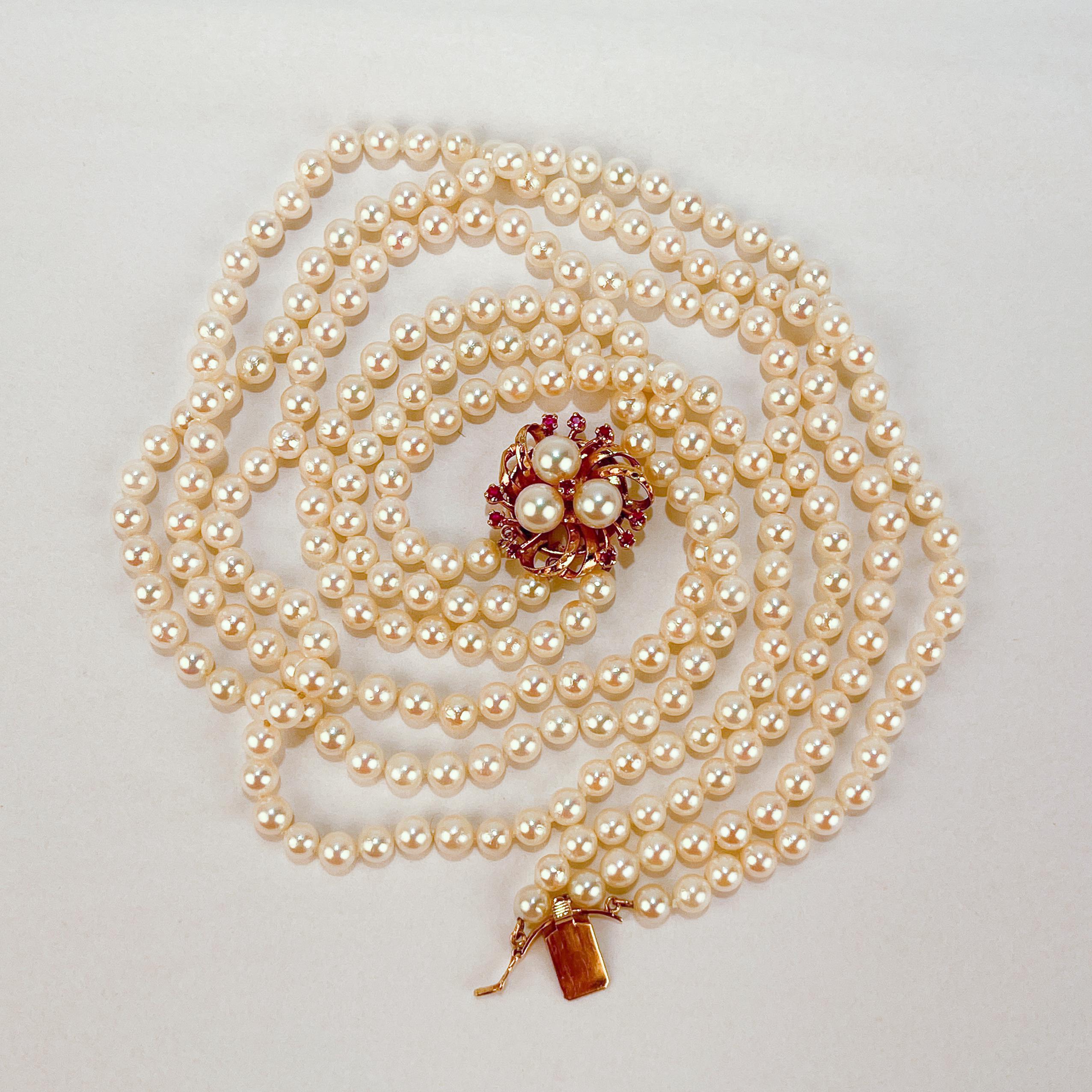 A very fine 3-Strand Akoya pearl necklace.

With a decorative 14k gold flower box clasp with prong set rubies that link the three strands of hand-knotted round white pearls on silk cord.

Created by Tasaki - one of Mikimoto's principal