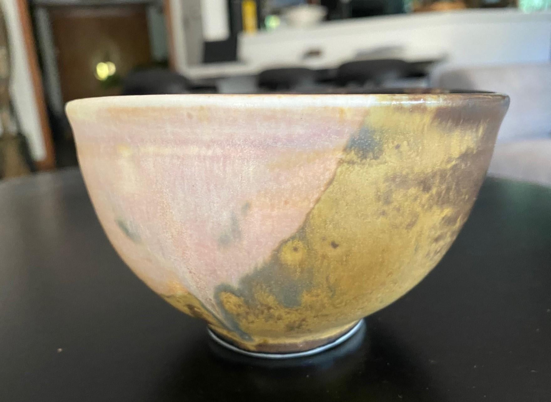 A beautiful and engaging Chawan tea bowl by famed Japanese Hawaiian American pottery master Toshiko Takaezu. The fired, somewhat oblong shaped bowl features a vast array of shifting, vibrant, and colorful glazes (with earth tones of browns, greens, 