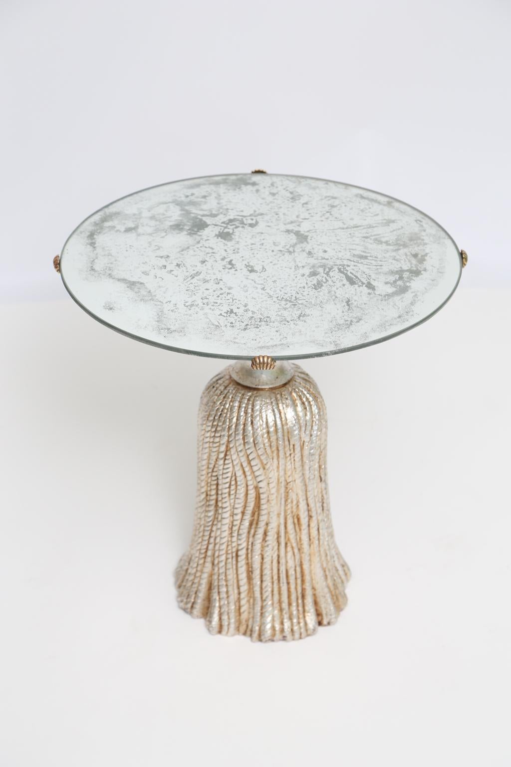 Accent table, having a round top of aged mirror, on a pedestal base of silvergilt metal, formed as an oversized tassel.

Stock ID: D2581.