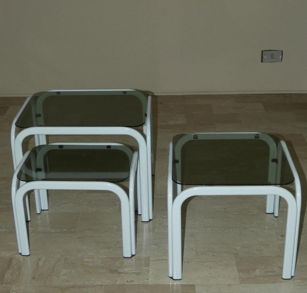 Ensemble de 3 tables basses  en métal peint en blanc avec des étagères en verre fumé. deux petites tables sont rectangulaires et empilables (la grande et la petite), tandis que la table moyenne est carrée.

Excellent état. Toutes les tables ont