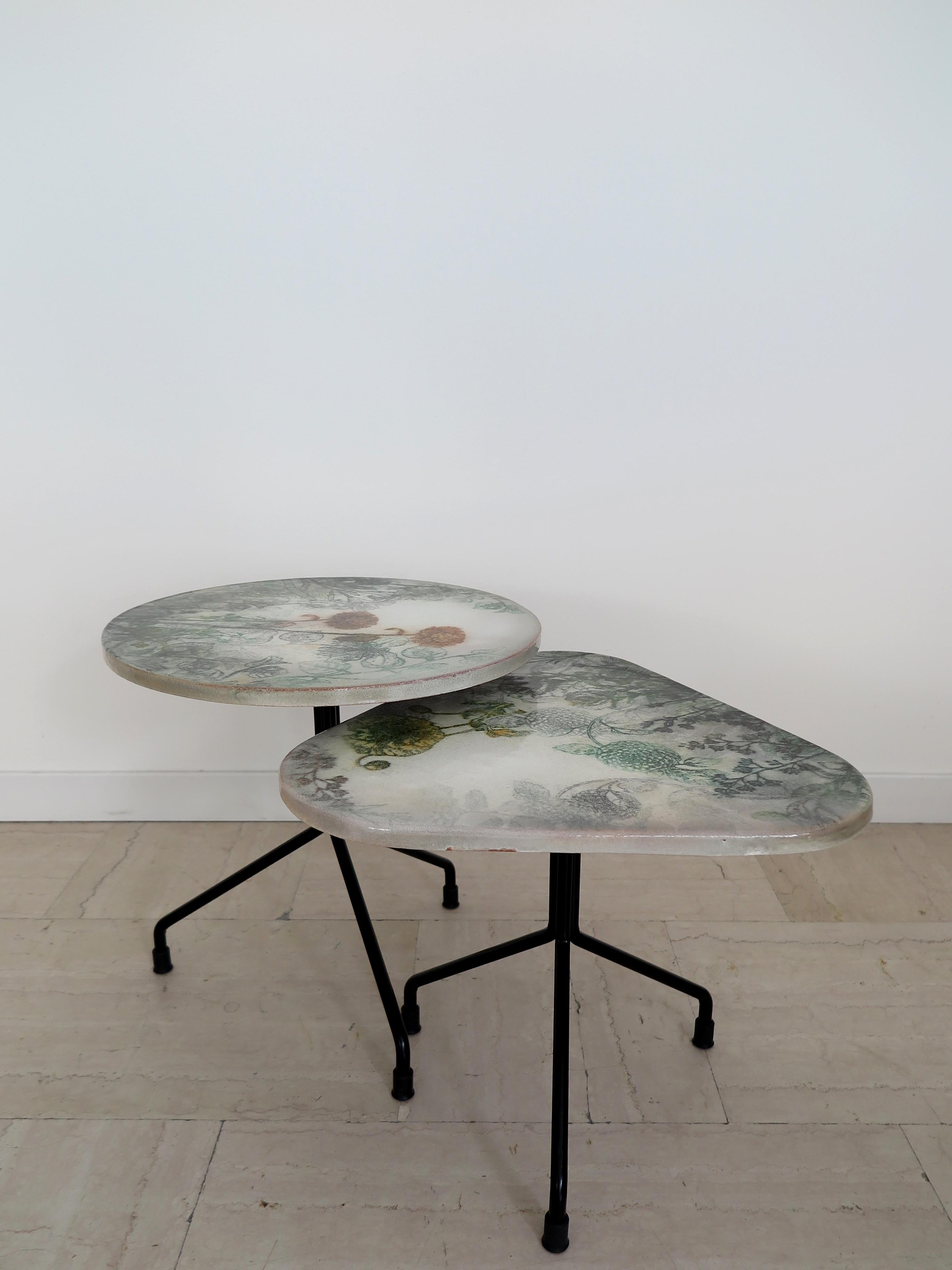 Coppia tavolini italiani contemporanei adatti sia per indoor che per outdoor, con top rotondo e triangolare in ceramica decorati a mano con disegni floreali realizzati a spruzzo; struttura del piede in metallo verniciato nero opaco.
Nuovo design
