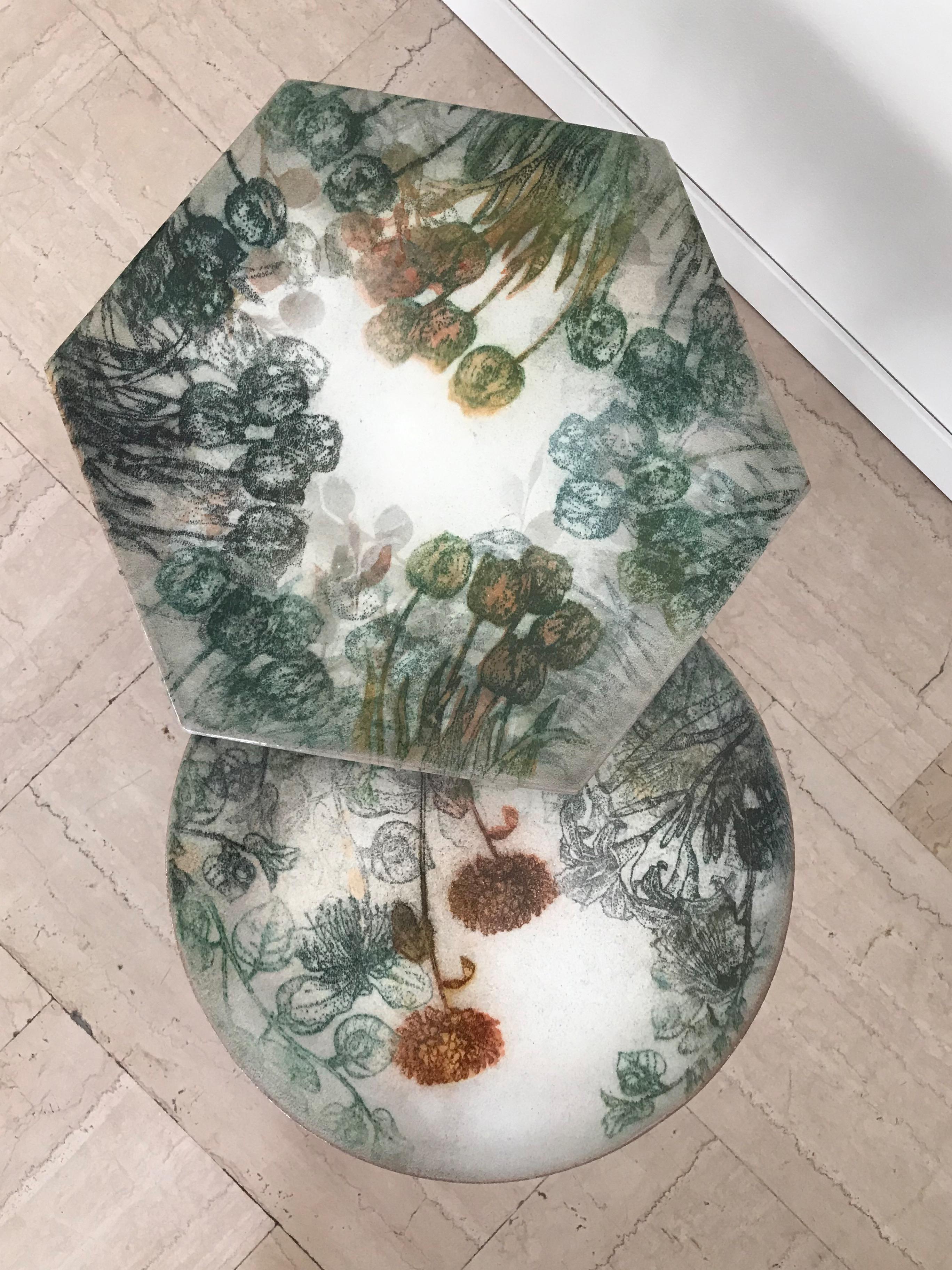 Coppia tavolini italiani contemporanei adatti sia per indoor che per outdoor, con top esagonale e rotondo in ceramica decorati a mano con disegni floreali realizzati a spruzzo; struttura del piede in metallo verniciato nero opaco.
Nuovo design