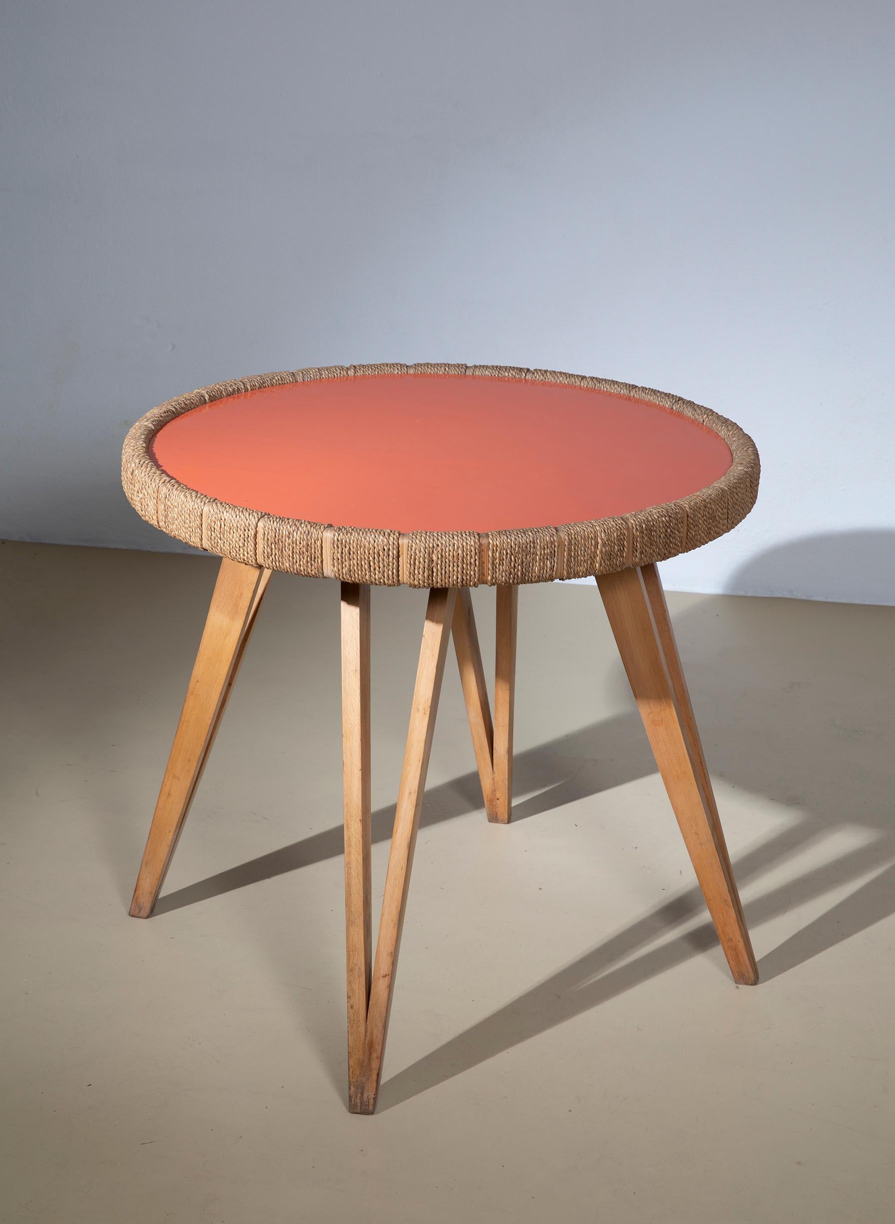 Tavolino disegnato da Augusto Romano negli anni '40. Il tavolino ha un piano in legno laccato lucido nei toni dell'arancio, inserito in una cornice di corda intrecciata e canna d'India alternate, e sorretto da 4 gambe affusolate a forma di triangolo.