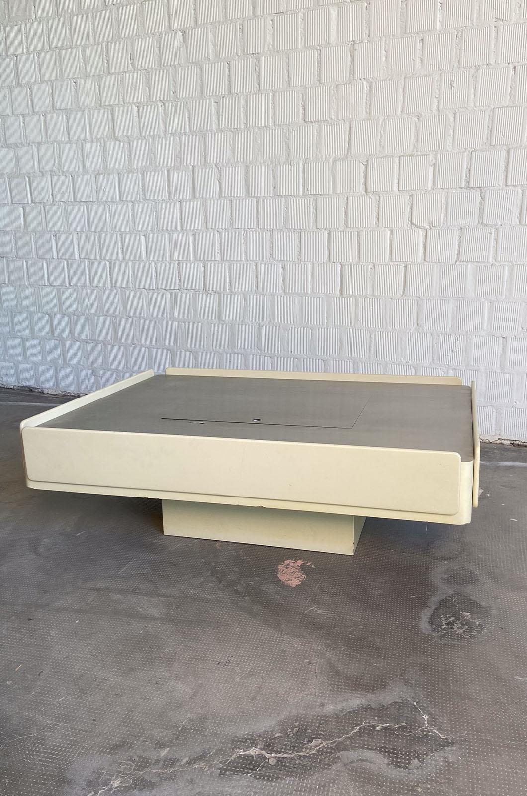 Coffee table designed by Vico Magistretti for Gavina Spa in 1963.
The table is raised off the ground by a wide central leg, which also serves as a storage compartment accessible by lifting the top cover. The perimeter of the table conceals