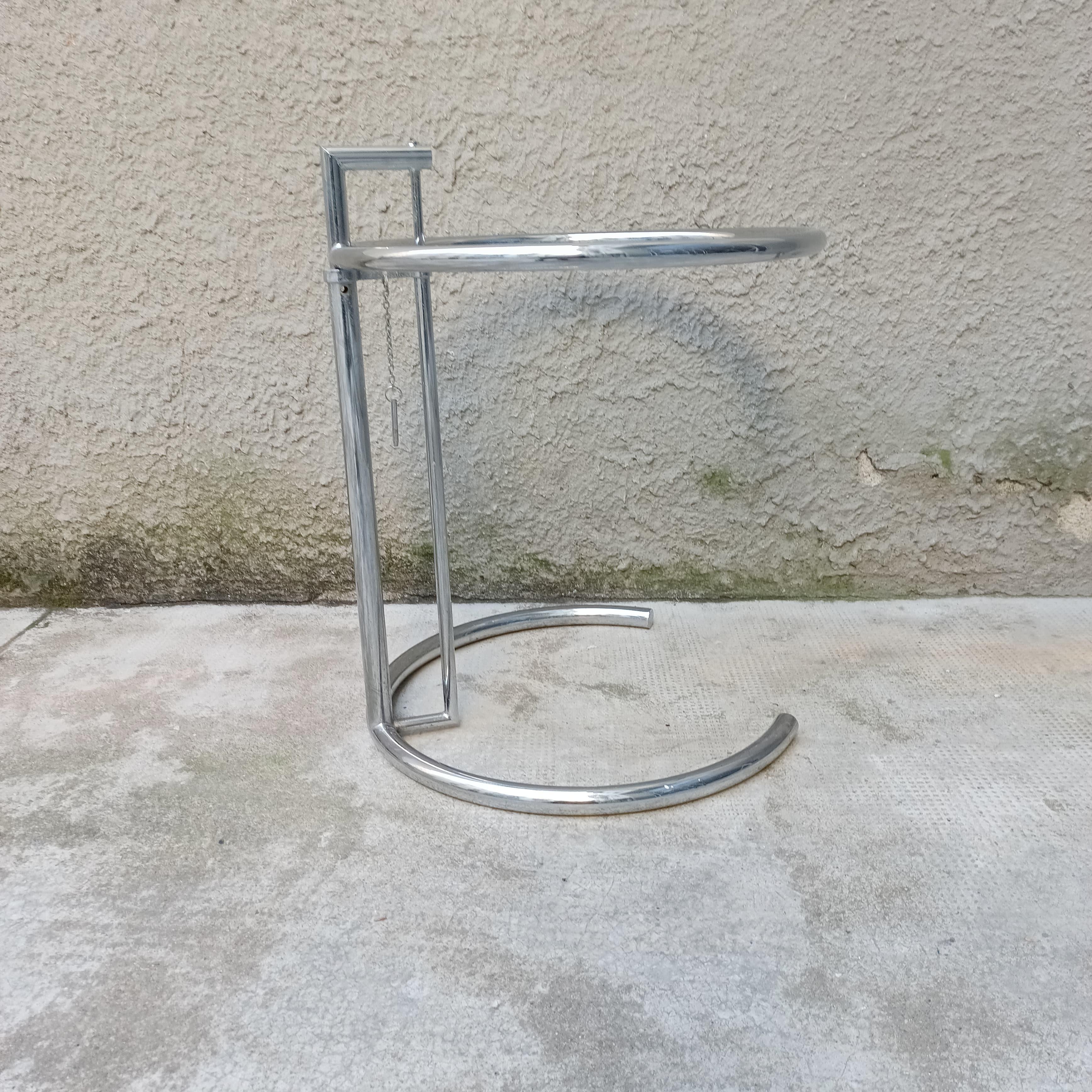 Couchtisch, inspiriert von Eileen Grays ikonischem Modell E1027, aus verchromtem Stahl, höhenverstellbar von 55 cm bis 100 cm.
Die Tischplatte ist aus Glas und hat eine leichte Absplitterung.
Eine Ergänzung, die man neben einem Sofa oder zwischen
