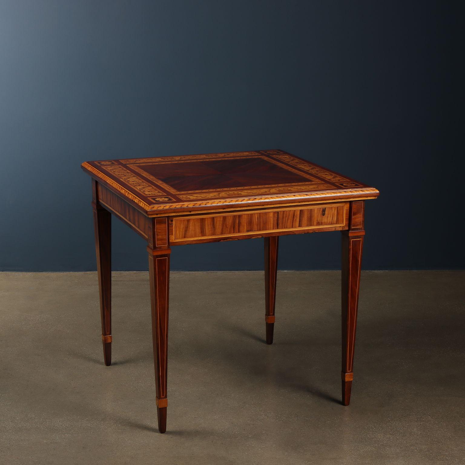 Tavolino da gioco a pianta quadrata con quattro gambe tronco piramidali; il piano inserito in una cornice è dotato di una molla di sblocco che permette, sia di toglierlo per accedere al vano contenitore inserito nella fascia, sia di ribaltarlo per