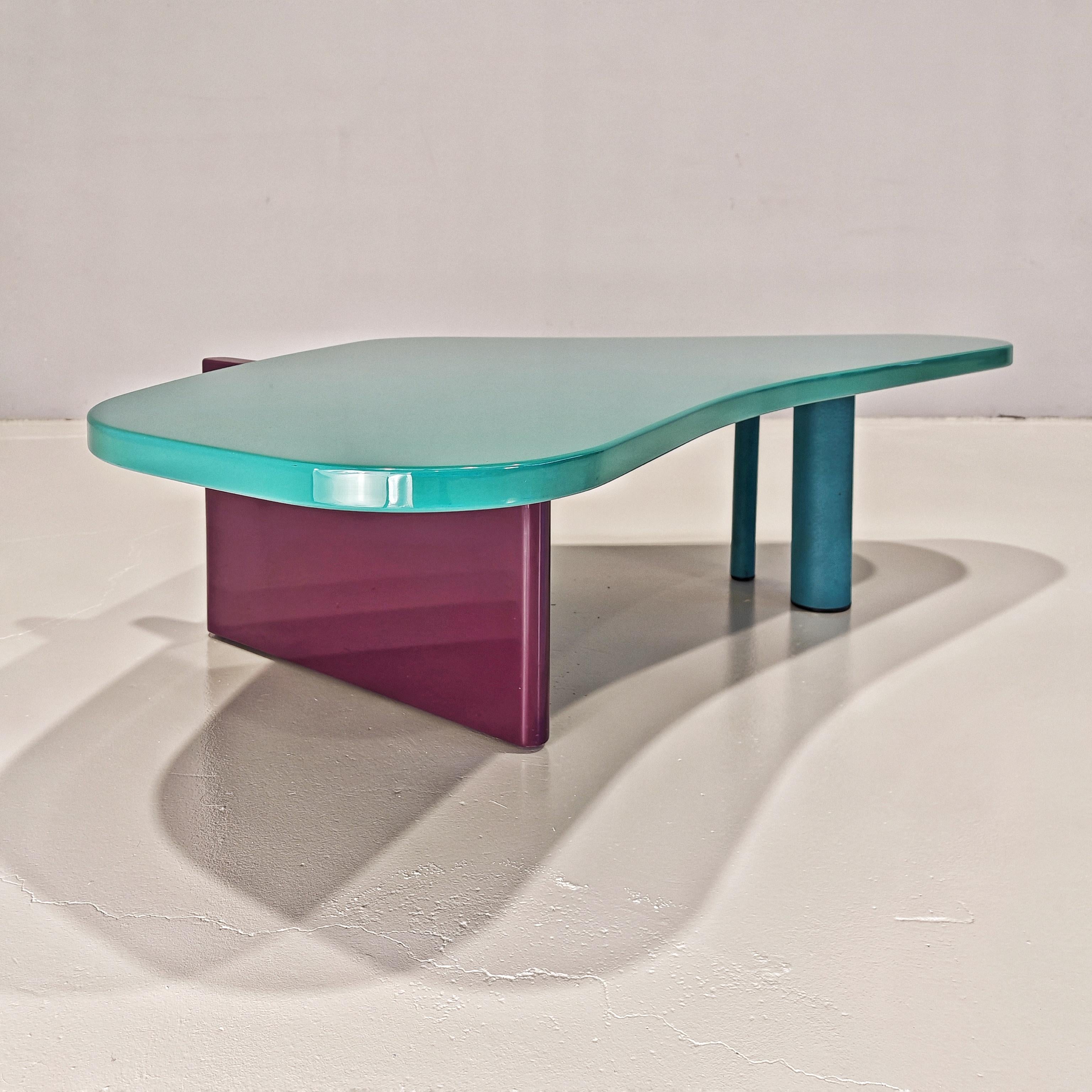 Splendido Tavolino da salotto prodotto negli anni 80 dalla Saporiti Italia. Piano di forma irregolare arrotondata laccato verde acqua marina, con base laccata viola e piedi di sostegno in vernice goffrata azzurra. Tipico esempio di design