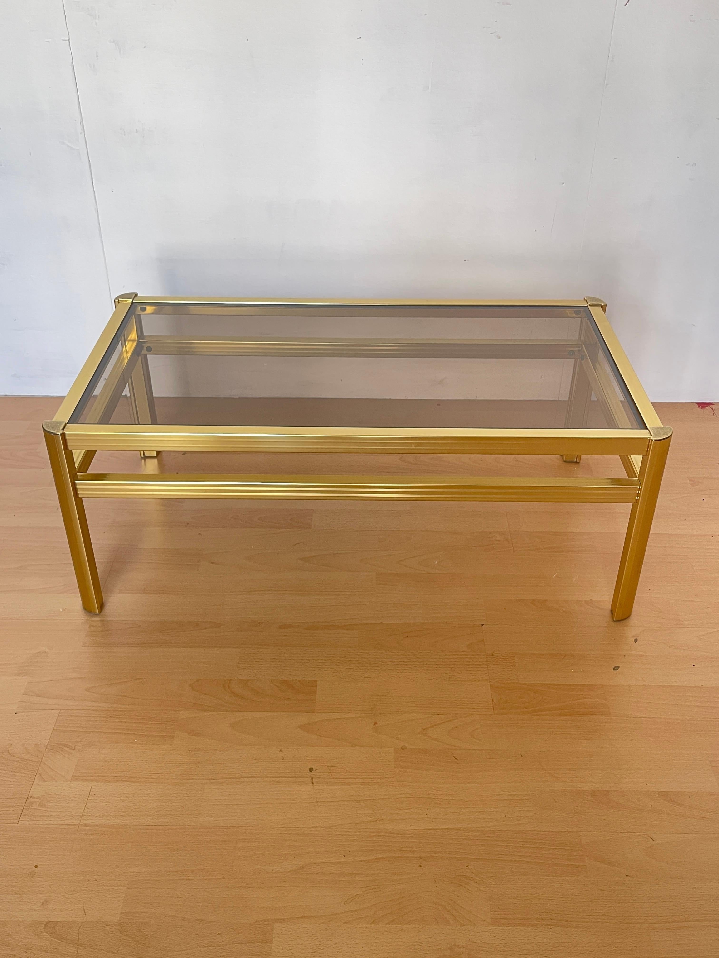 Elegante mesa de centro de estilo vintage moderno, perfecta para ambientes sofisticados y glamurosos.
La estructura de latón dorado pulido aporta brillo y prestigio, mientras que la encimera de cristal ahumado proporciona un efecto refinado y
