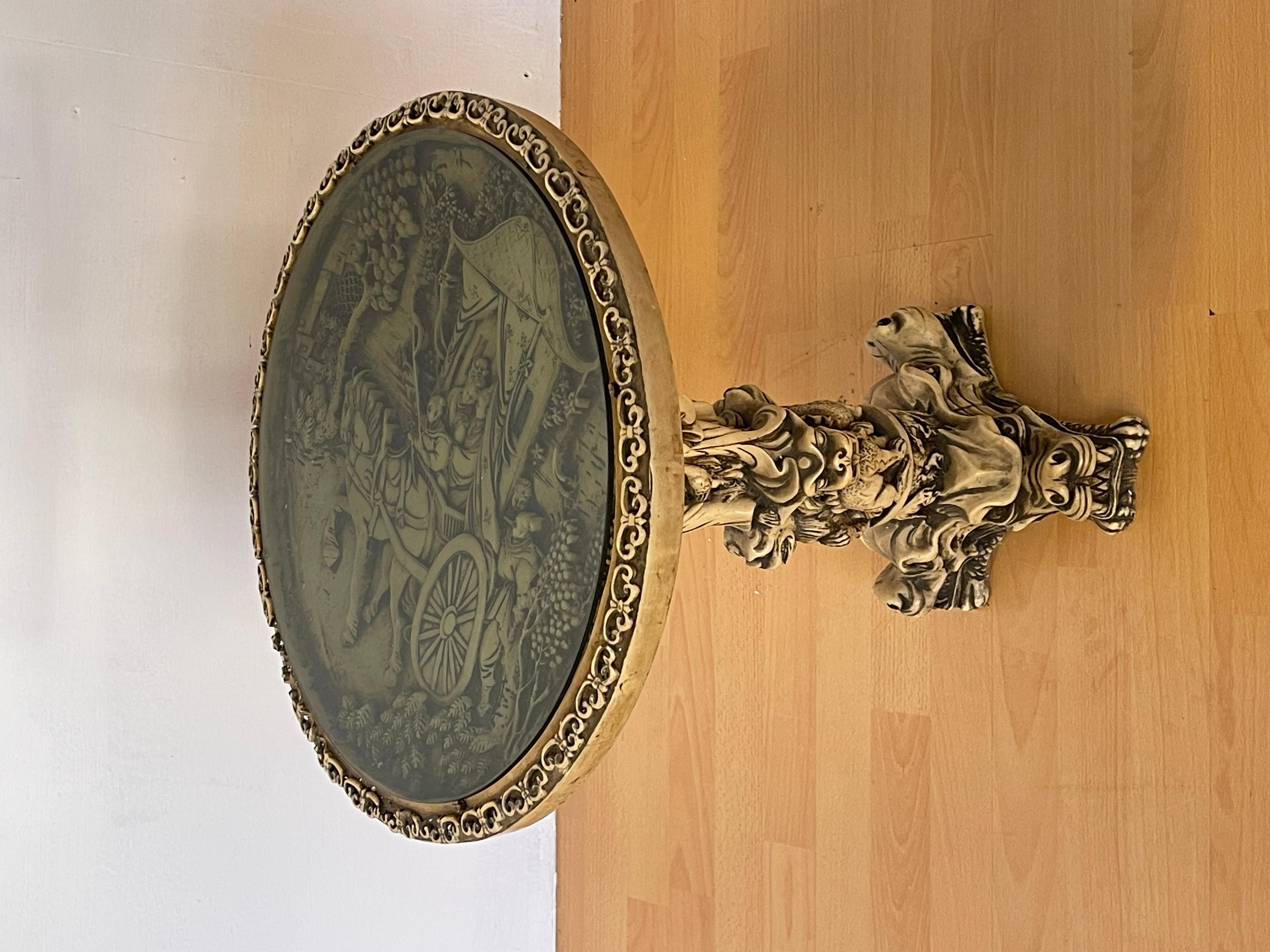Un affascinante tavolino d’arredo in stile orientale, caratterizzato da una base scolpita con dettagli di dragoni e figure mitologiche. Il piano tondo è rifinito con una cornice decorativa e presenta una superficie in vetro che protegge un’incisione