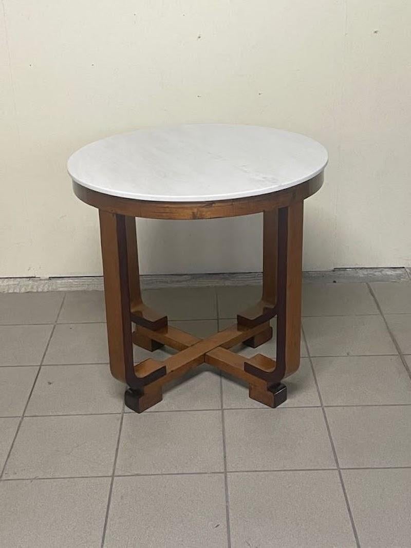 Un bel tavolo di servizio o tavolo da caffè tondo degli anni '30 in piena art déco.

Struttura in legno di noce con piano in marmo bianco.

Le gambe formano un movimento ad intreccio molto piacevole ed armonico.

Completamente restaurato in modo