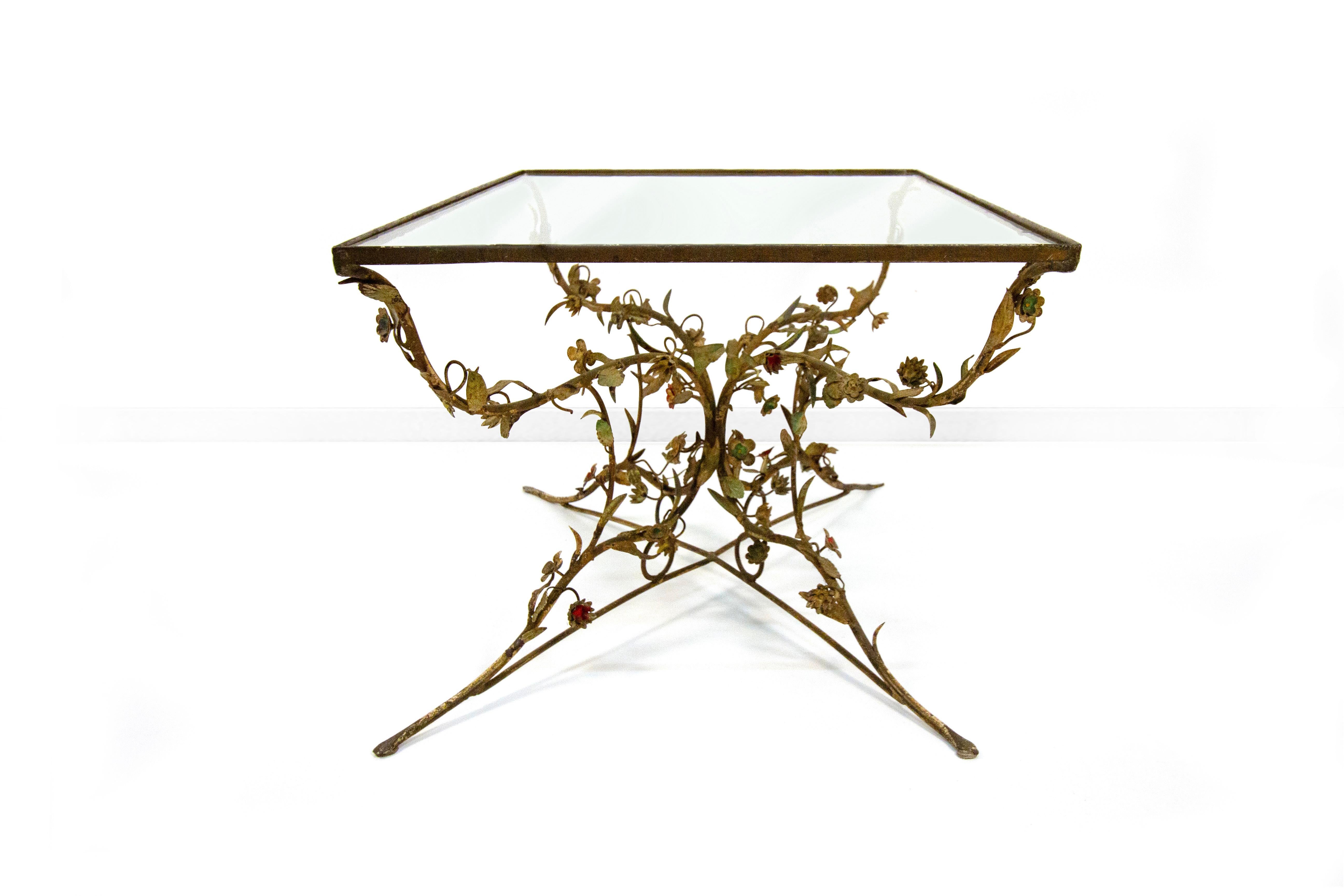 Tavolino in ferro battuto e vetro, XX secolo, piano rettangolare in vetro trasparente sorretto da quattro montanti in ferro battuto a volute decorate da piccoli fiori e foglie in lamierino, cm 49x92x61