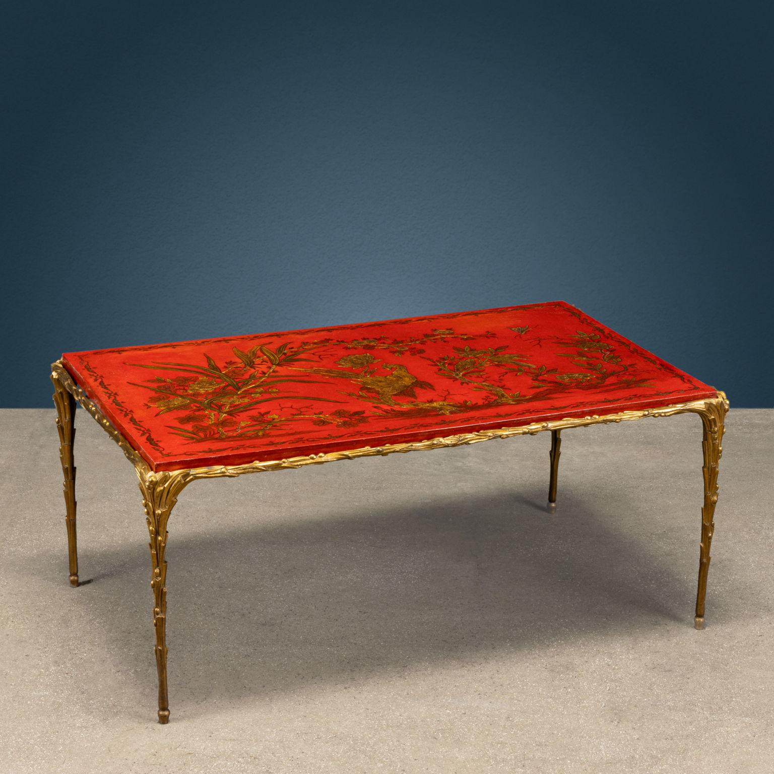Petite table en bronze doré et travaillé avec des feuilles de laurier et des petites baies, plateau de fabrication chinoise en bois laqué rouge peint en or avec un oiseau au centre de la scène, encadré par des éléments végétaux.