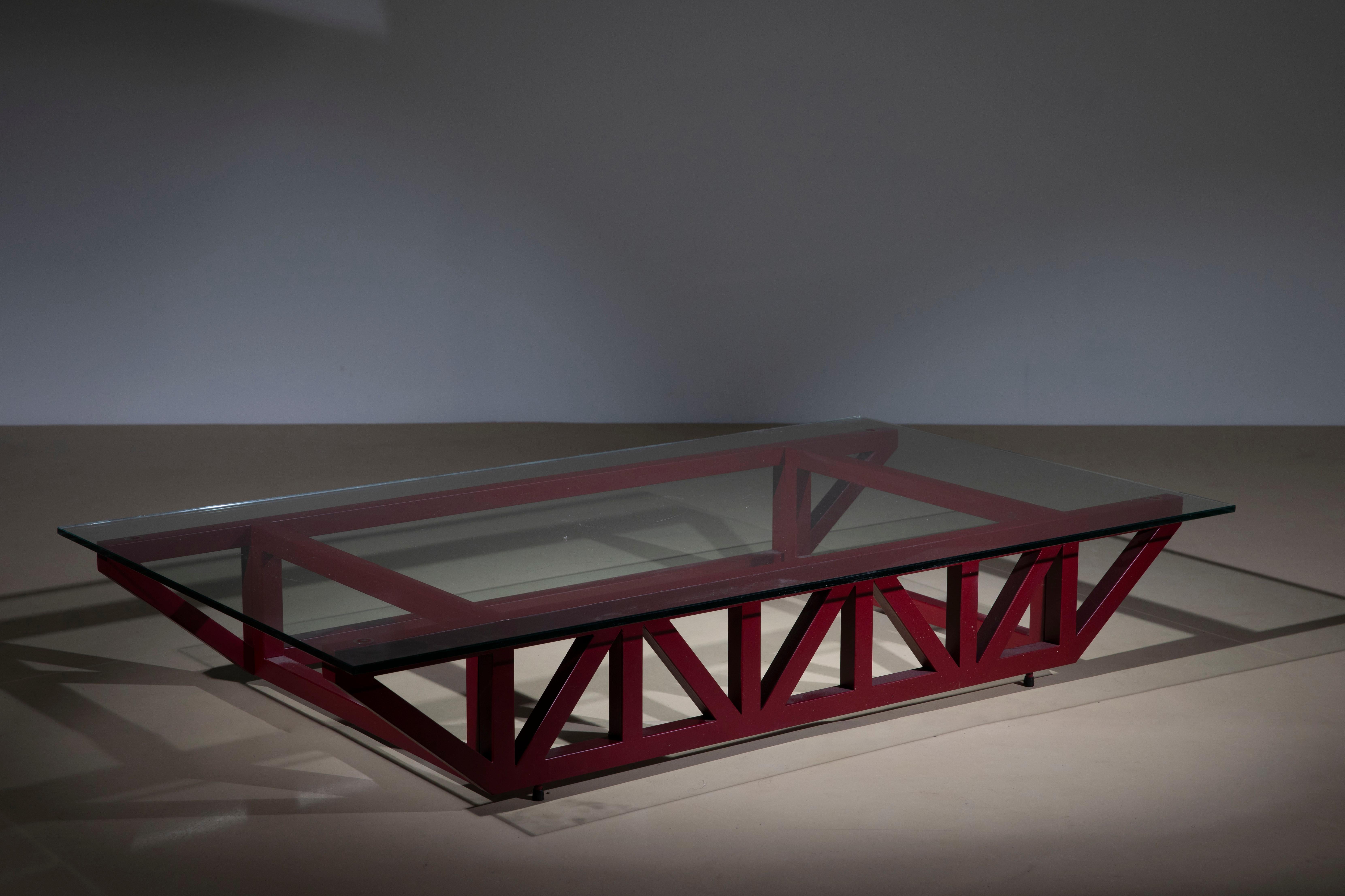 Particolarissimo tavolino in stile postmoderno, manifattura italiana degli anni '80, presenta una base reticolata in acciaio laccato nei toni del rosso e un piano di vetro temperato.
