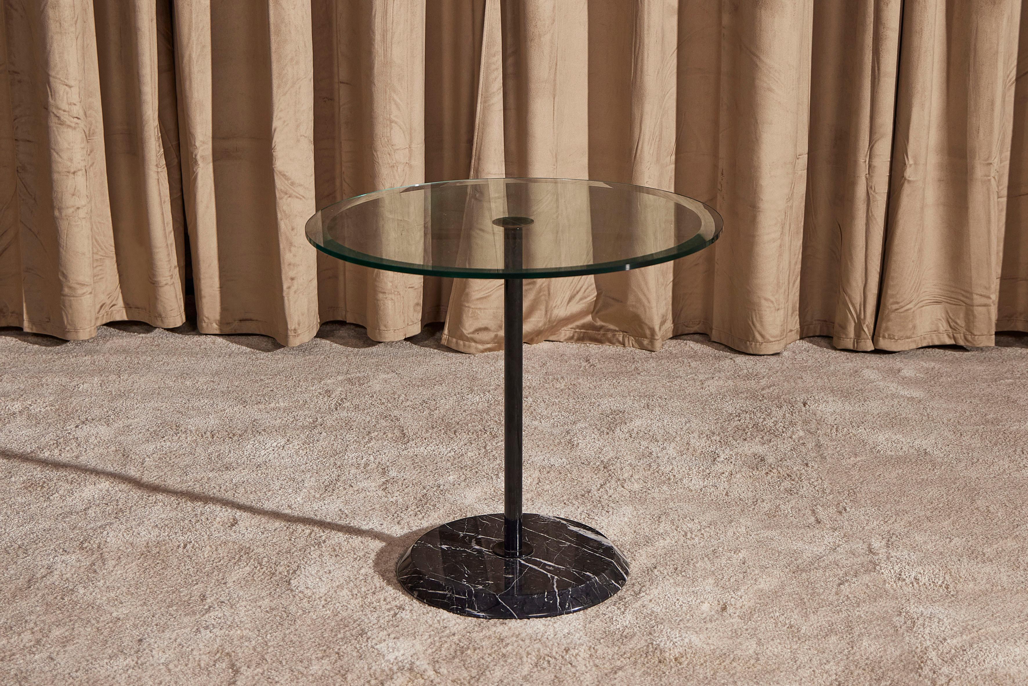 Elegante mesa de centro de los años 80 con tapa redonda de cristal biselado, base de mármol Marquina negro y pie de hierro pintado. Su diseño minimalista lo hace adecuado en cualquier entorno, también como mesa auxiliar o mesilla de noche. El estado