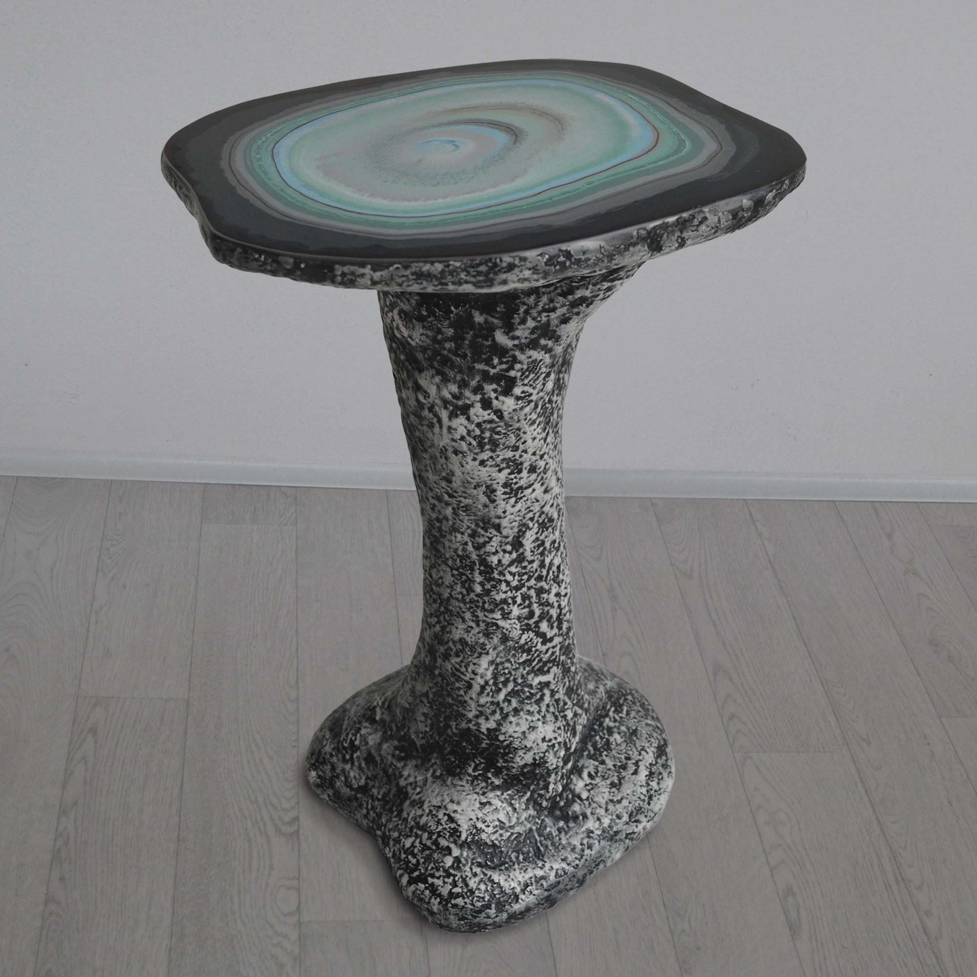 Table d'appoint pour canapé réalisée en une seule pièce et caractérisée par le contraste entre la surface lisse et polie du plateau en scagliola  et l'aspect brut et multiforme de la tige, créant un dialogue entre l'élégance et l'artisanat, offrant