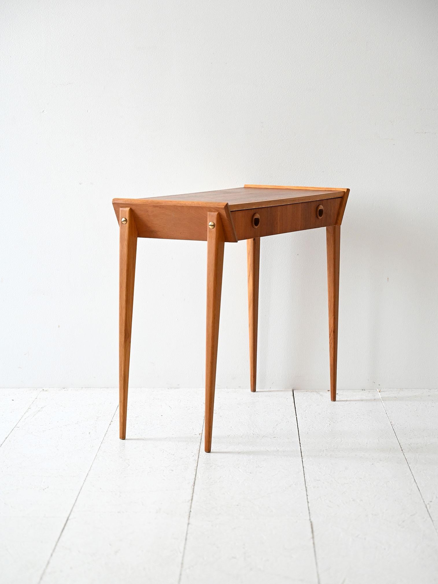 Tavolino in teak anni ’60 con cassetto, maniglie rotonde intagliate e struttura dalle linee decise.

Tavolino scandinavo vintage anni ’60 in teak con struttura geometrica slanciata e gambe appuntite. Il frontale ospita un cassetto con doppia
