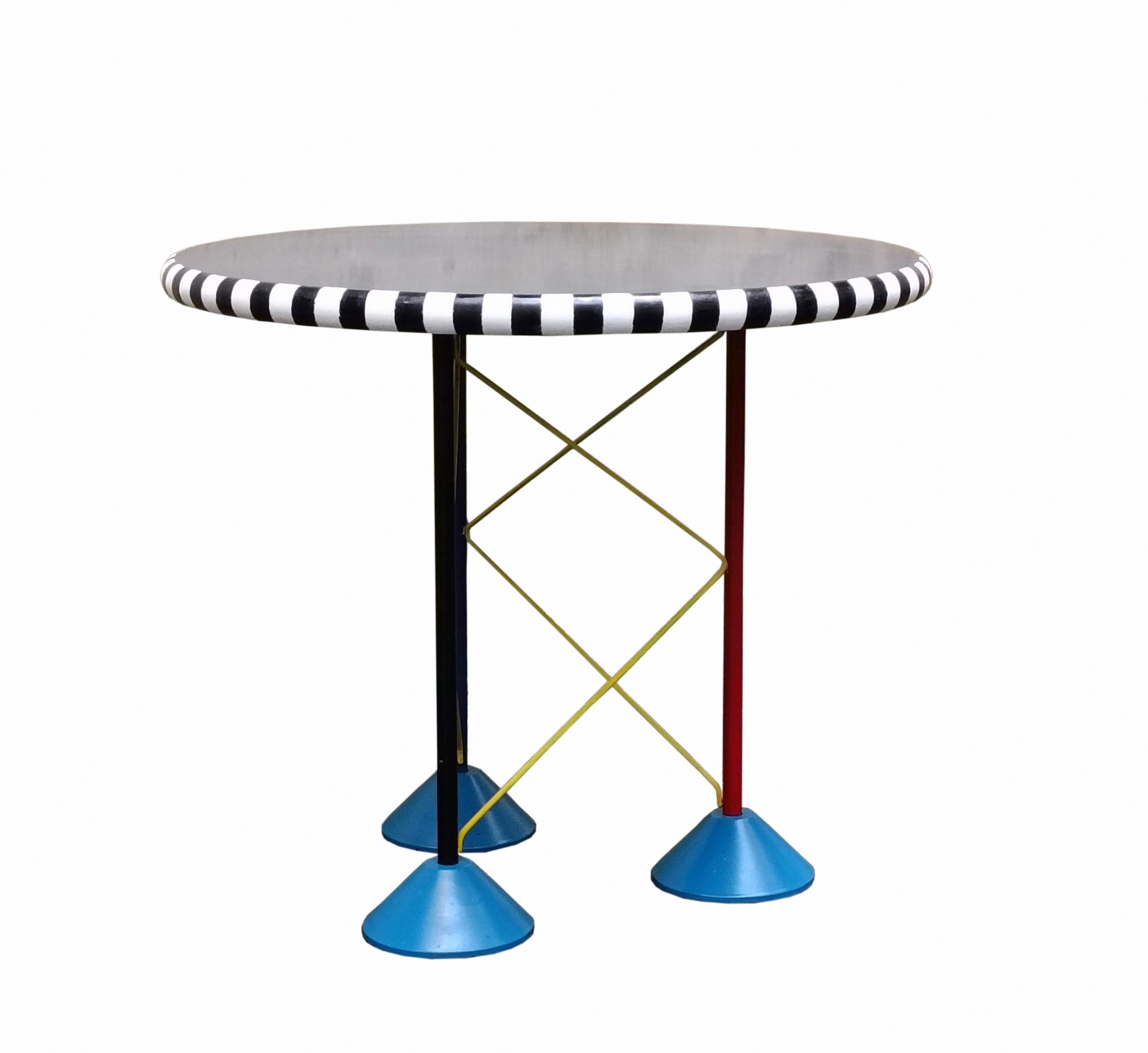 Circular-shaped coffee table with a smooth finish.
The border is decorated with a black and white striped pattern, which gives an eye-catching and dynamic effect.
 The table legs are three, thin and colored red, black and blue 
connected to each
