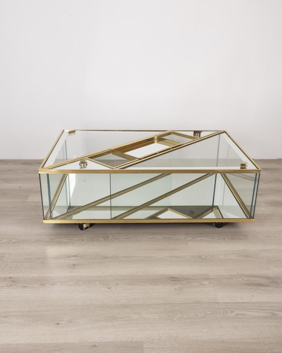 Table basse à roulettes, cadre en laiton doré, cristal et miroirs, avec plateau extractible, briquet et cendrier, design italien, années 1960.

ÉTAT : En bon état, peut présenter des signes d'usure au fil du temps.

DIMENSIONS : Hauteur 39 cm ;