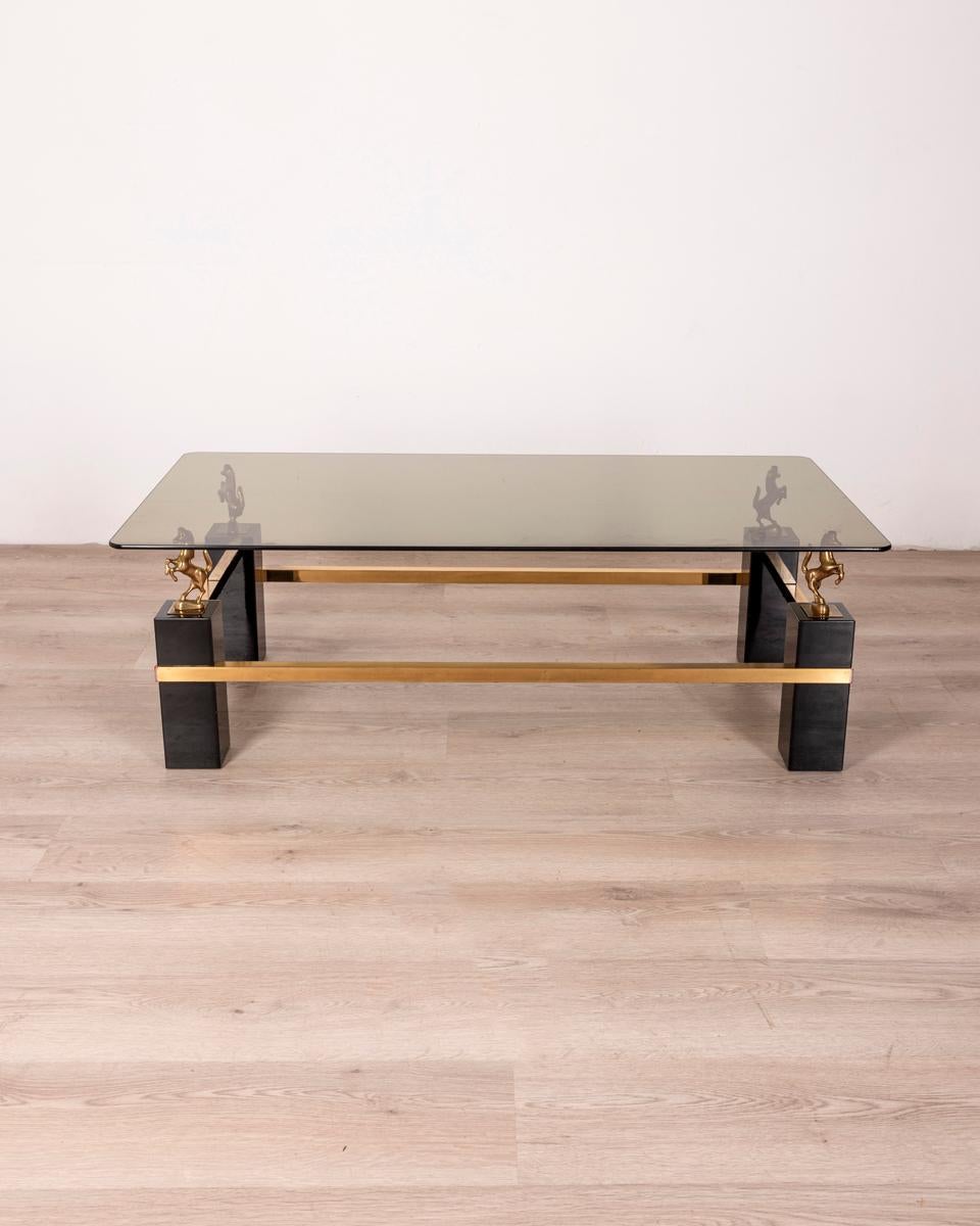 Table basse avec structure en bois laqué noir et laiton doré, plateau en verre fumé reposant sur quatre tréteaux dorés.
Design Maison Charles, années 1970.

ÉTAT : En bon état, avec des signes d'usure dus au temps.

DIMENSIONS : Hauteur 40 cm ;
