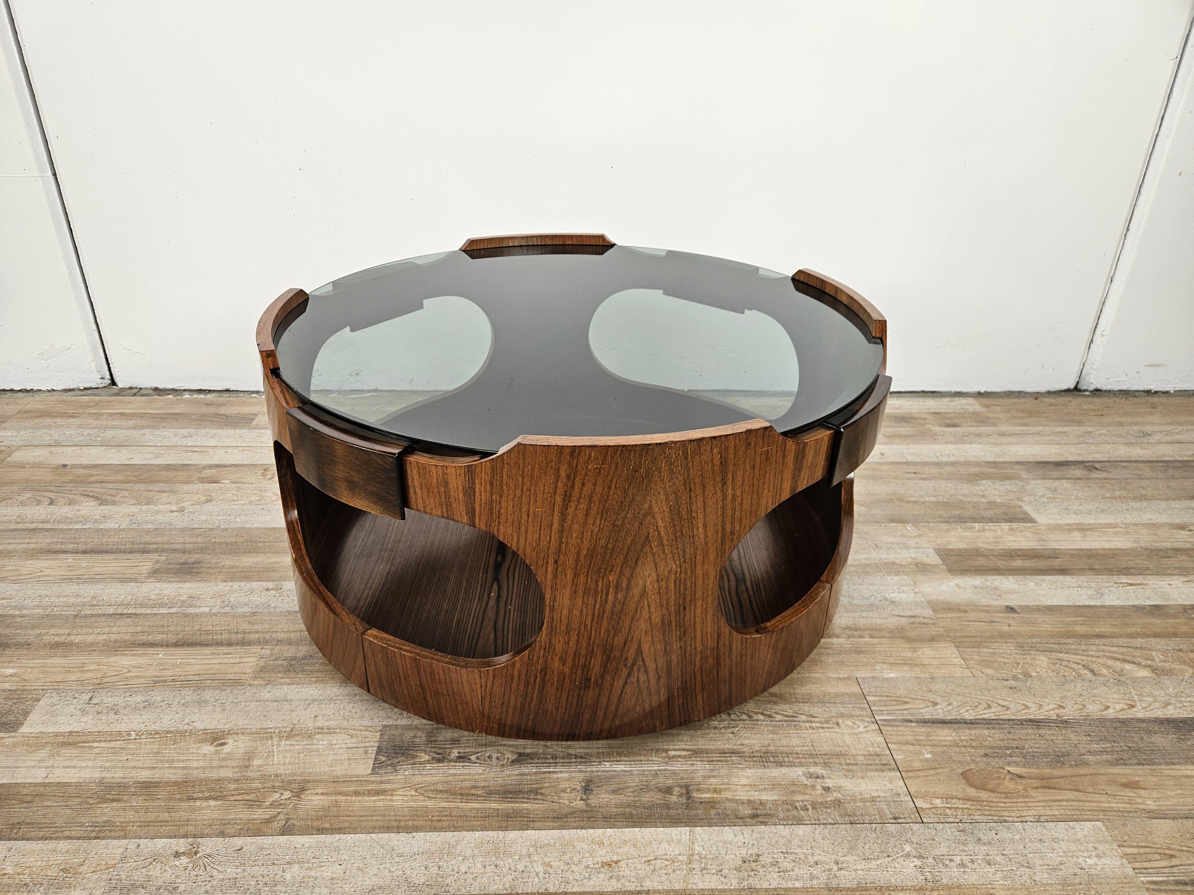 Tavolino da caffè vintage dei primi anni '70 impiallacciato teak e legno di noce con piano rotondo in vetro fumè e tre ruote poste alla base.

Elemento d'arredo moderno, ideale per soggiorni salotti o ingressi di casa.

Normali segni d'usura dovuti