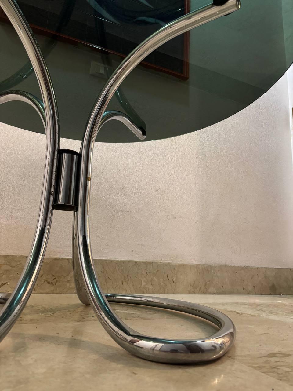 la table en question présente un design qui rappelle les créations de Giotto Stoppino ou de Gastone Rinaldi, deux éminents designers italiens du XXe siècle.

Caractéristiques principales :

Plateau en verre : Le plateau est en verre foncé,
