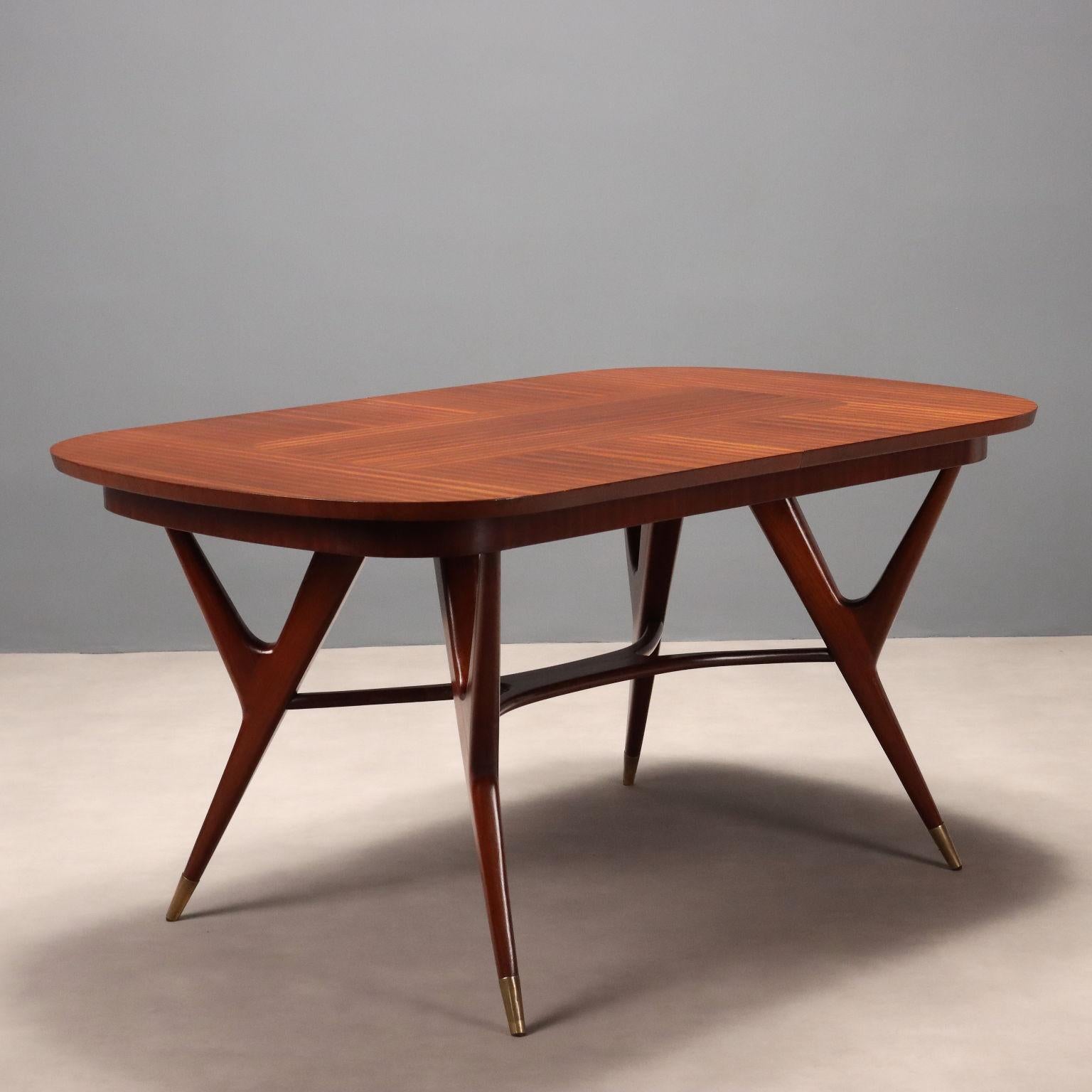 Elegante tavolo da pranzo di manifattura italiana del XX secolo con piano ovale allungabile e gambe dalla forma sinuosa che terminano con puntali in ottone; in legno impiallacciato mogano.