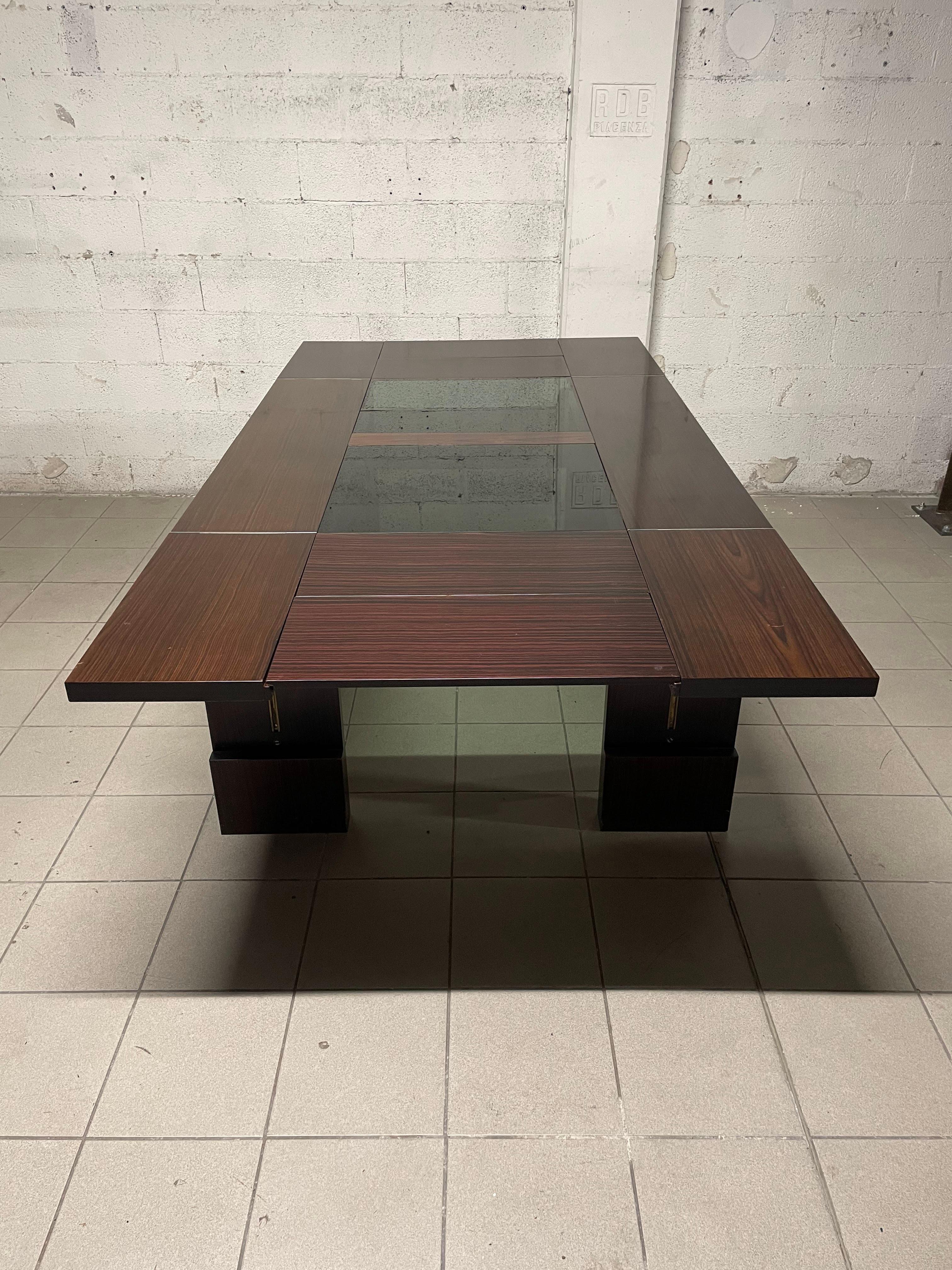 1970s extendable dining table.
Rosewood frame with central crystal inserts that make the aesthetics of this table lighter.

An easy mechanism allows two flaps to be raised, and from the sides the extensions can be pulled out.
All opened it reaches a