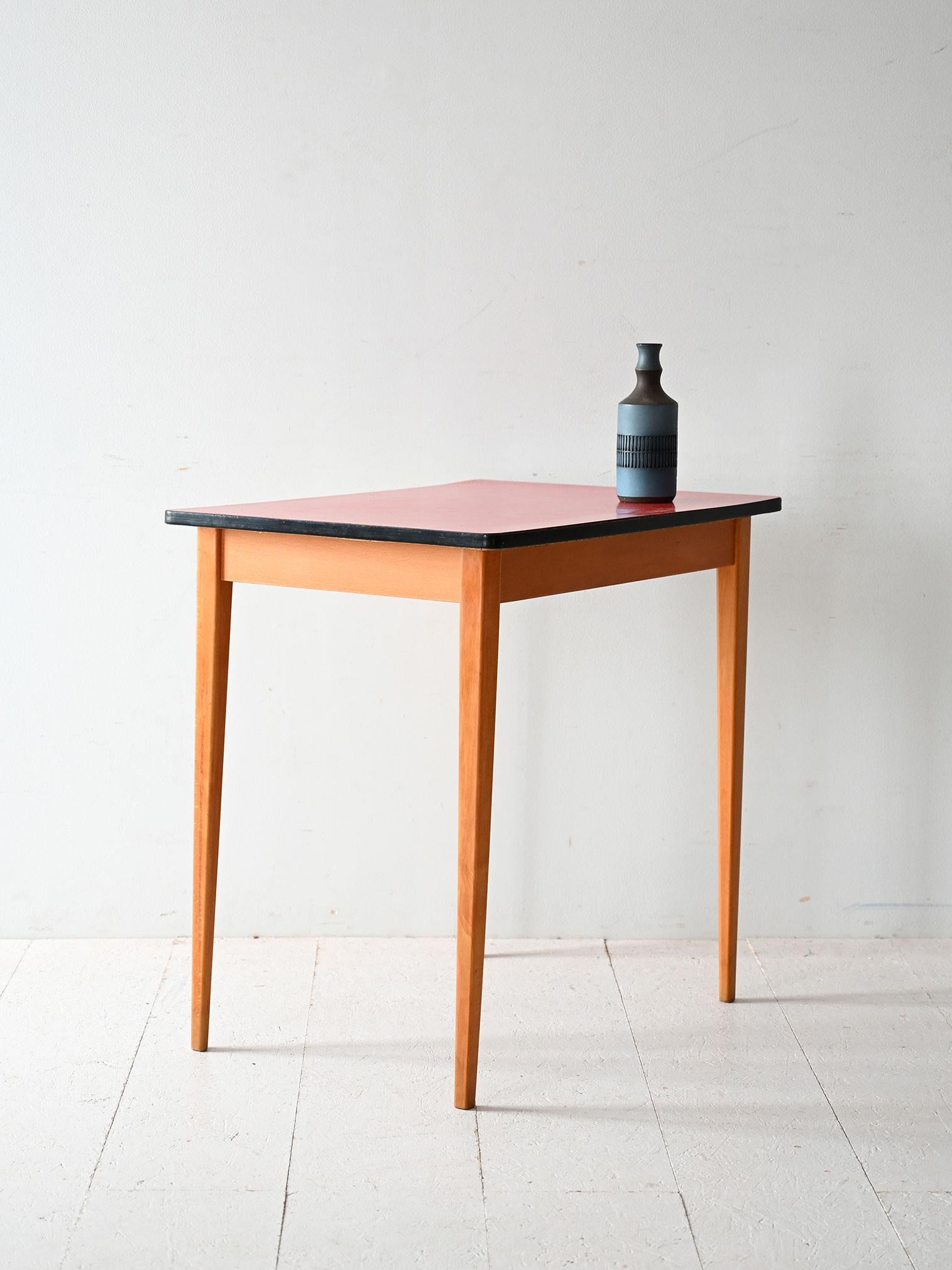 Scandinavian table from the 1960s with tapered wooden legs and red Formica top with contrasting black edge.

Vintage Scandinavian table from the 1960s featuring a slender frame with tapered solid wood legs. The top is covered in red formica, a