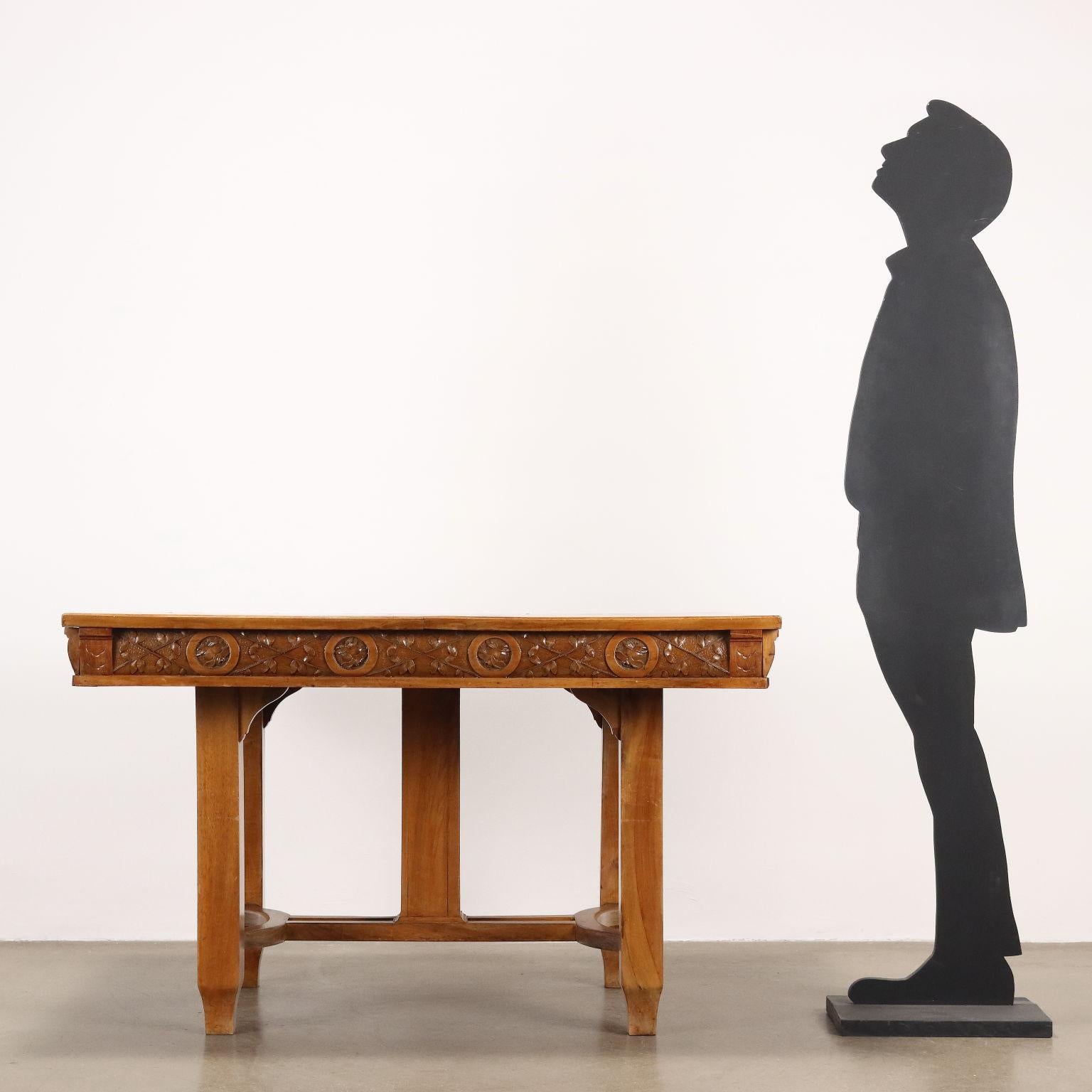Mesa Art Nouveau de sección cuadrada en madera de cerezo, hoja y tallas florales en la banda inferior. Tablero apoyado sobre cuatro patas unidas por una cruz y una pata central, listones laterales desmontables para sostener un par de