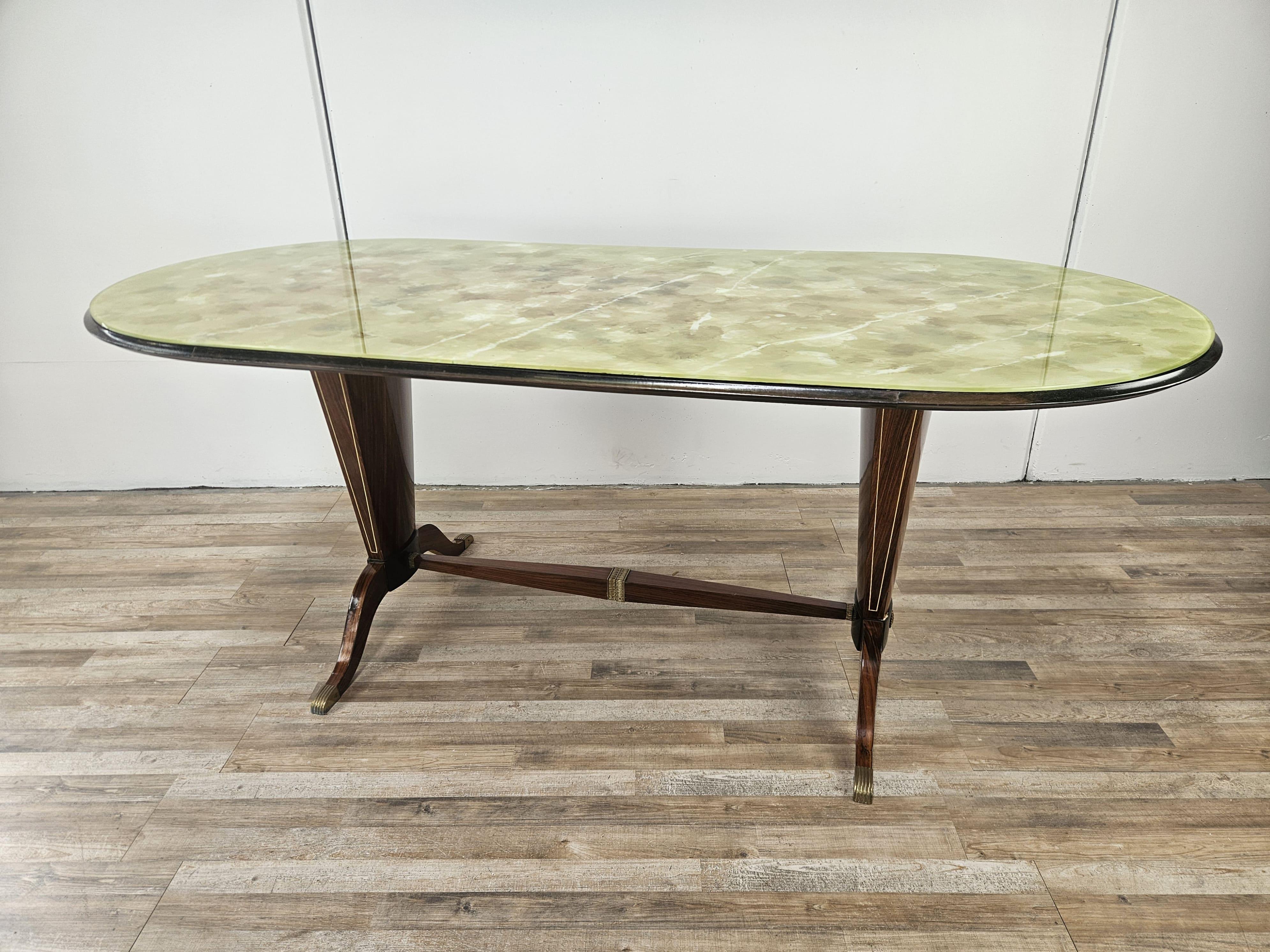 Elegante tavolo da pranzo italiano Mid Century anni '50, fine e compatto con dimensioni ideali per ogni tipologia di ambiente.

Il tavolo ha un piano in vetro con colori e decorazioni lungo tutta la superficie, contornato da una struttura in ebano e