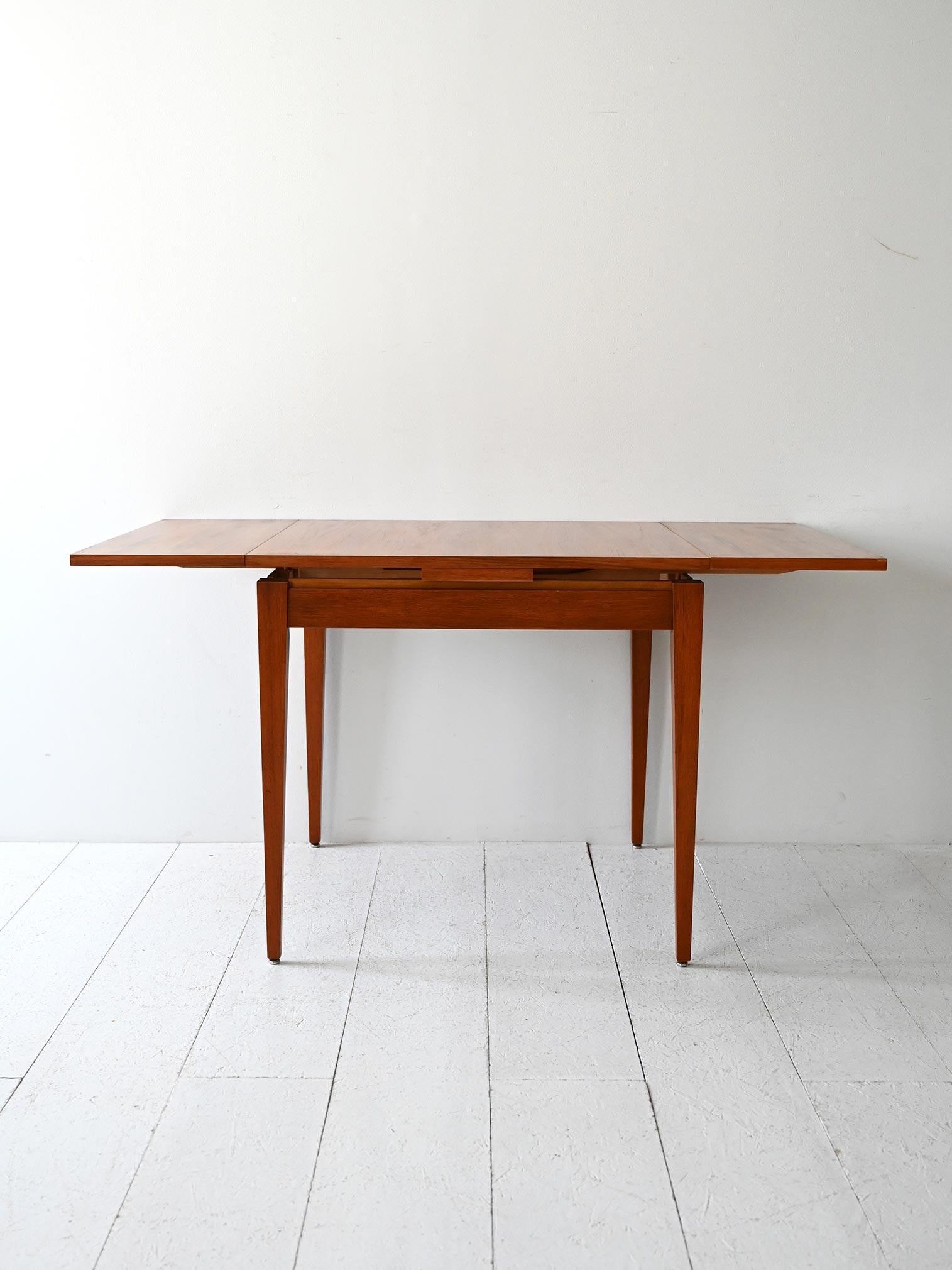 Tavolo quadrato in teak con due allunghe laterali. Estensione totale fino a 140 cm.

Tavolo scandinavo vintage risalente agli anni ’60, con struttura in teak e piano quadrato estensibile tramite due allunghe laterali pieghevoli. Il legno presenta
