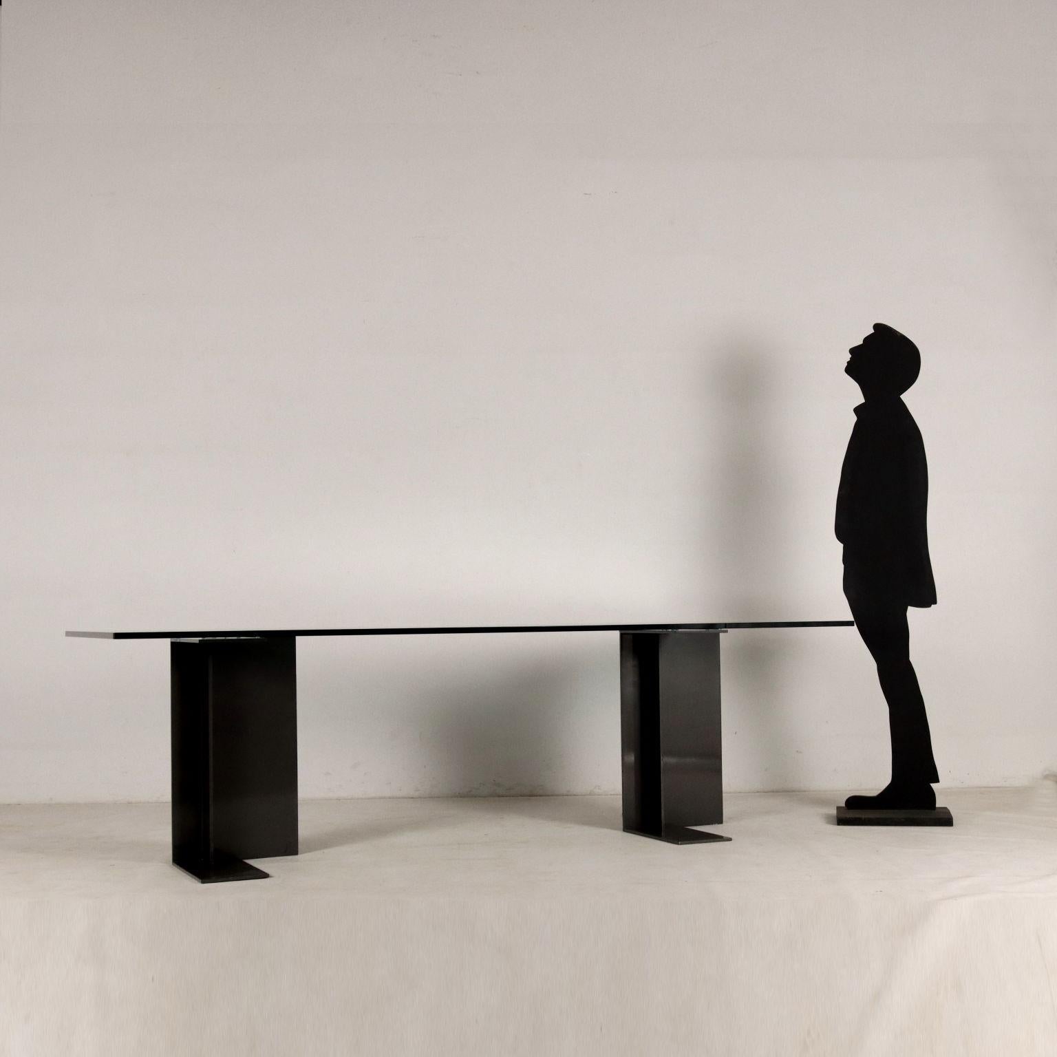 Grande tavolo con piano in cristallo sostenuto da due gambe in metallo. Buone condizioni.