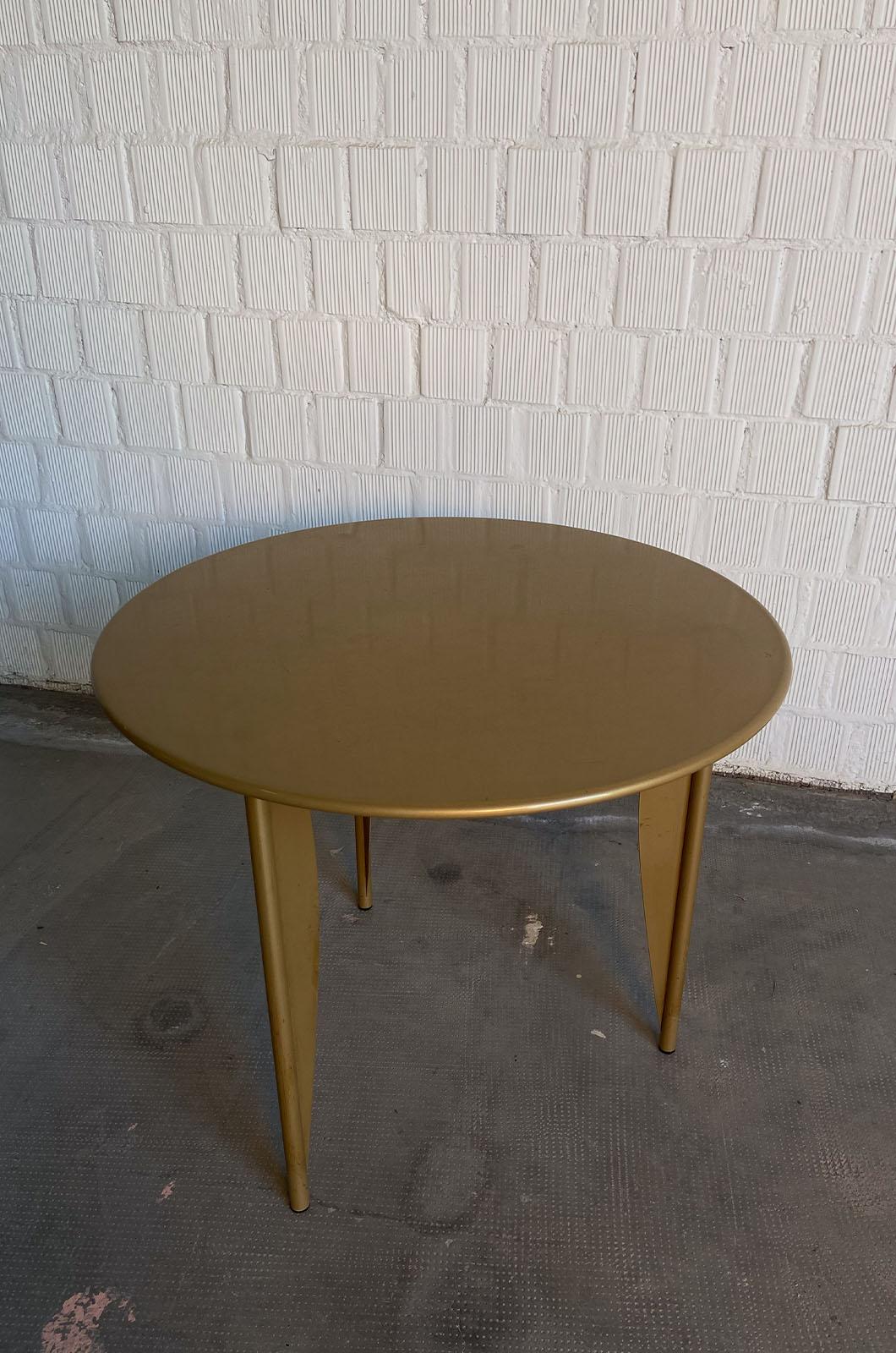 Tisch, entworfen von Philippe Starck & Aleph Ubik für Driade im Jahr 1984. Der Tisch hat eine leichte Struktur: Die drei Stützbeine sind klappbar und erlauben es, die Tischplatte darauf zu schließen. Der Tisch ist vollständig aus Metall gefertigt
