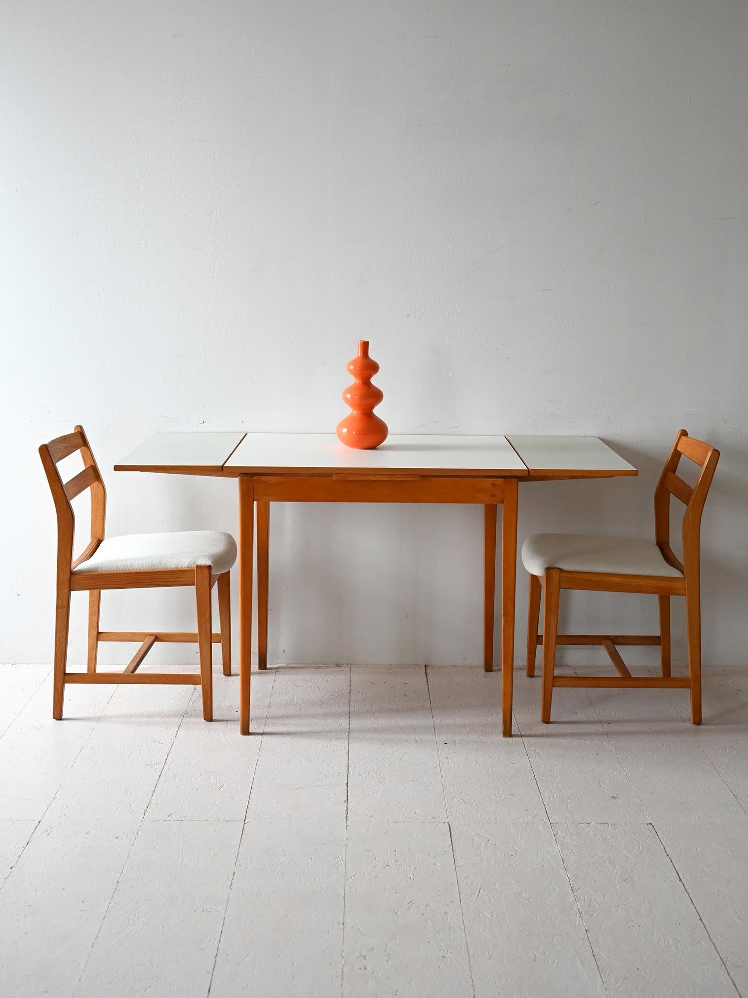 Table from the 1950s/60s with teak frame, light-colored formica top, and two retractable side extensions.

Essential lines and warm materials characterize this vintage Scandinavian table, made between the 1950s and 1960s. The teak frame supports a