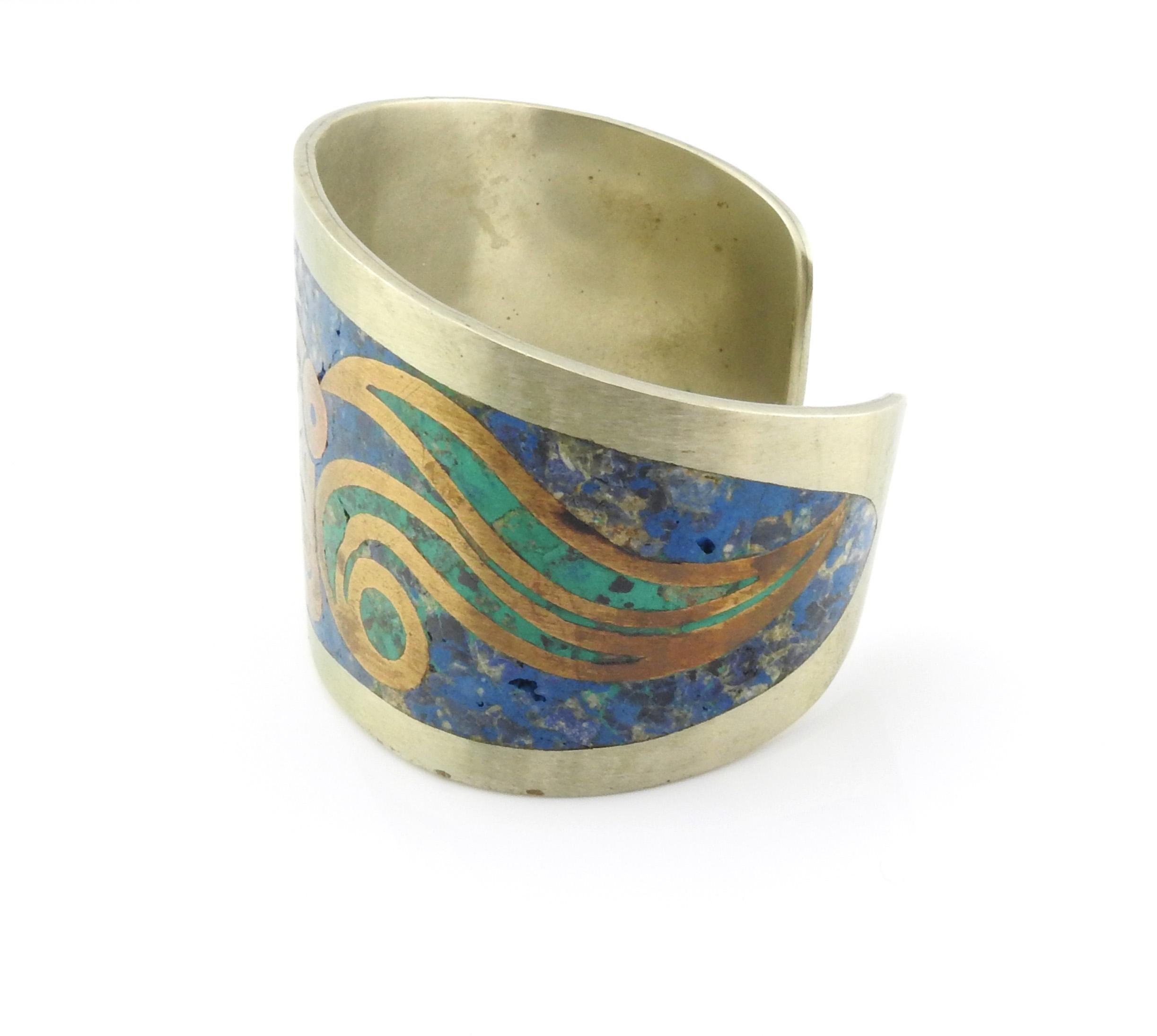 Taxco Mexico Alpaca  brass turquoise & lapis lazuli inlay cuff bracelet. Brass design on top of inlay features what looks like a god/deity face with swirls.

Marking: ALPACA MEXICO TAXCO.

Measures approx. 5 1/2