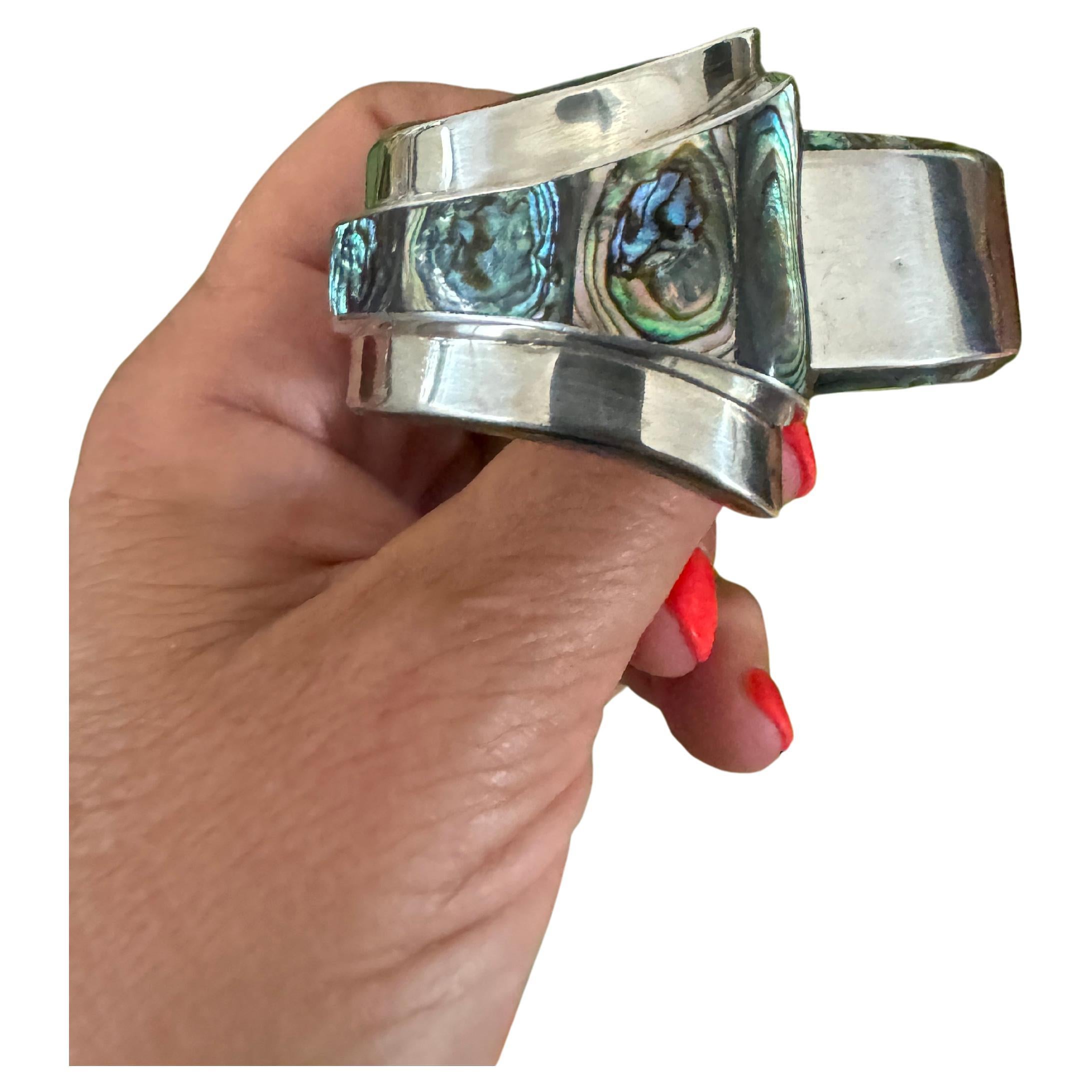 Si tratta di un superbo bracciale Clamper in argento sterling del 1965 circa, realizzato da Alfredo Villasana di Taxco, Messico, un bracciale modernista a cerniera con inserti in abalone. Villasana lavorò per Spratling e Aguilar prima di aprire un