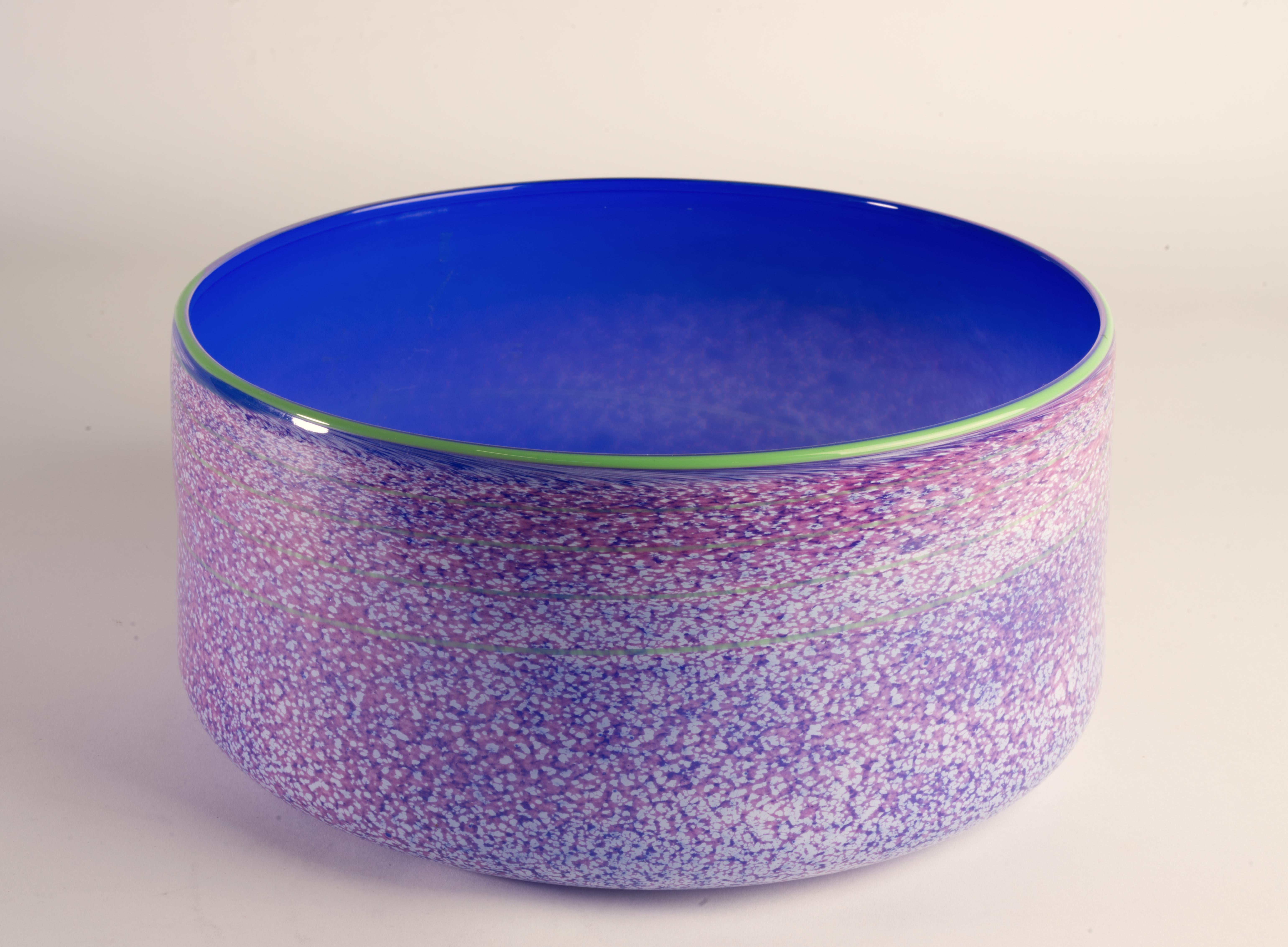 Hand blown art glass bowl has speckled exterior in shades of off-white, burgundy, and light blue, separated by light green rim from cobalt blue interior. A thin green line swirls throughout the piece, guiding the eye and adding movement and interest