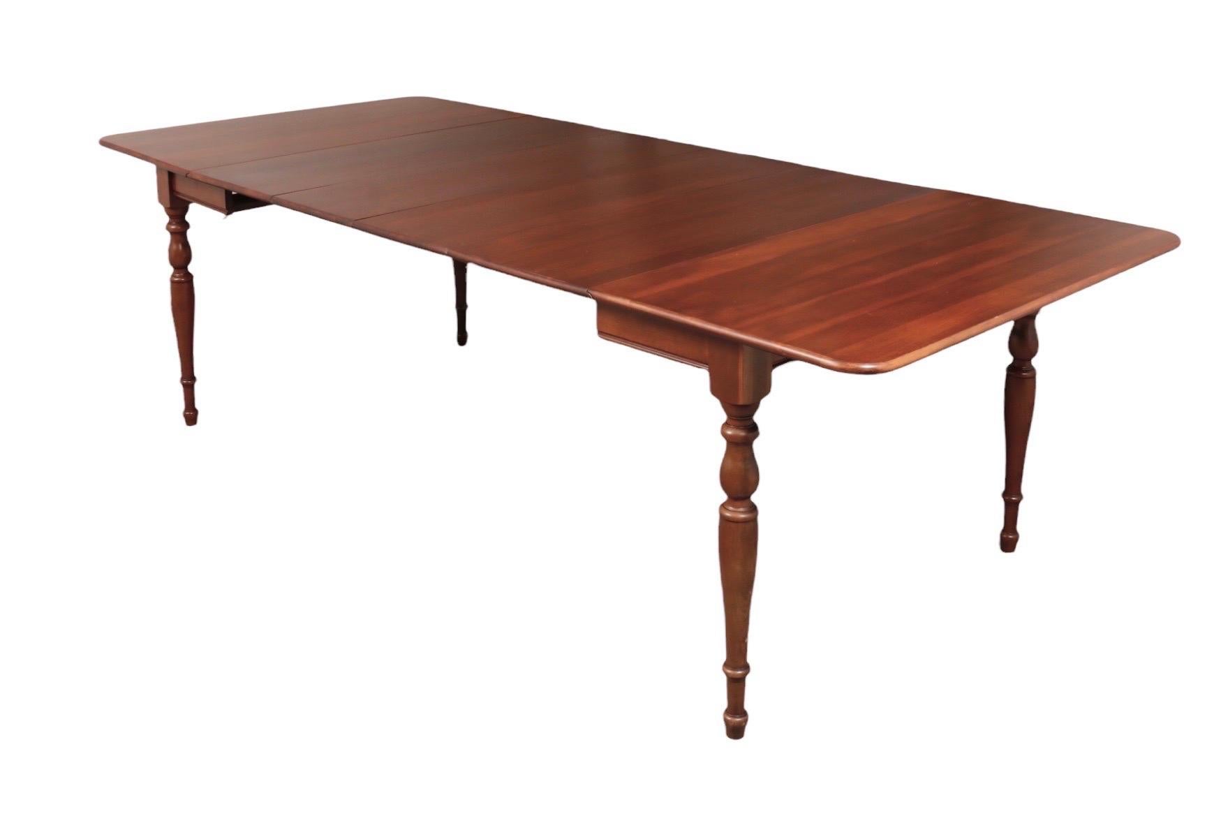 A traditional drop leaf dining table made by Taylor-Jamestown, dating from the 1960’s. Made of solid cherry wood, the table extends with two drop leaves and two additional leaves to comfortably seat ten. Supported by turned legs finished with blunt
