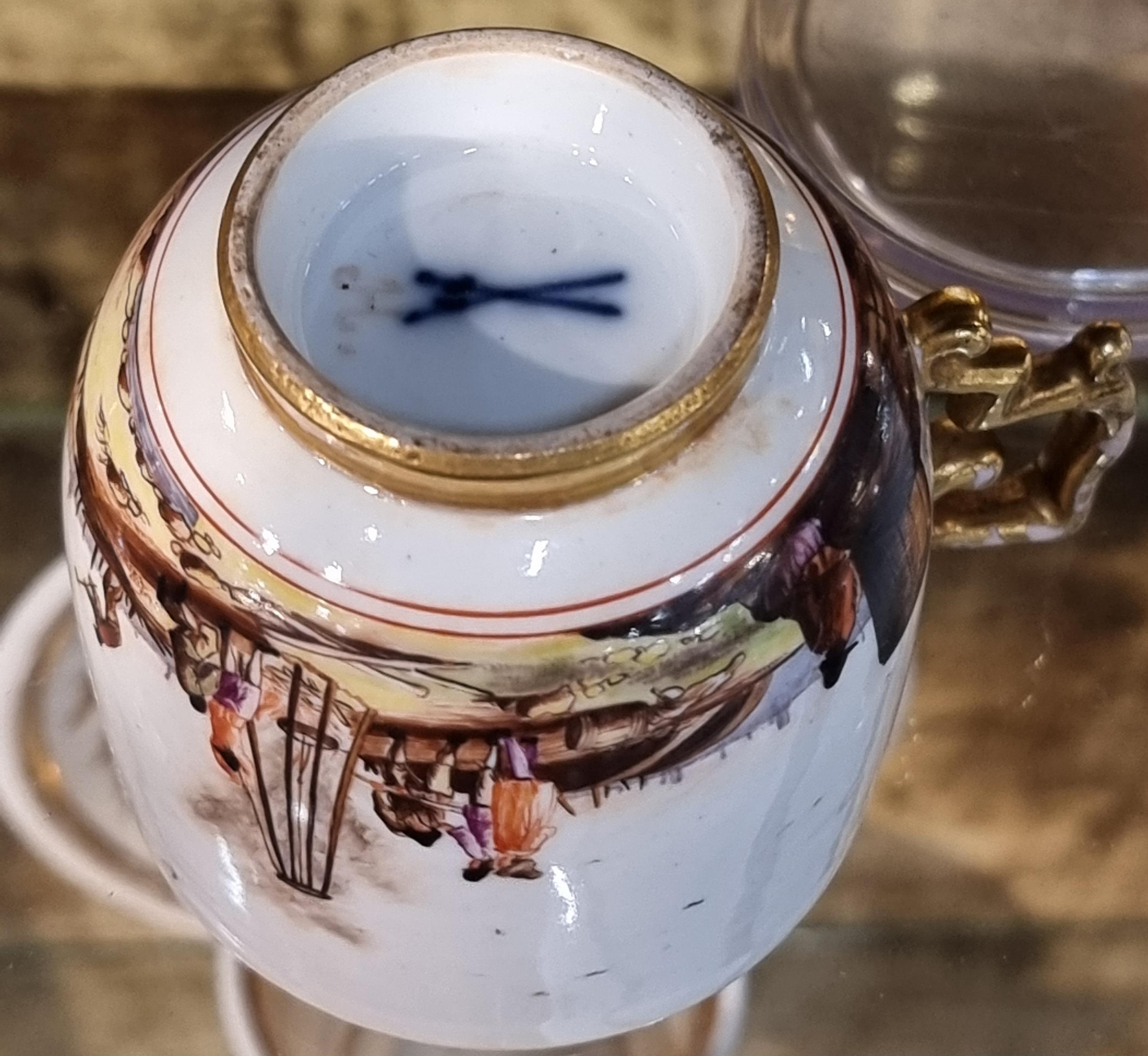 Elegante tazzina con piattino in porcellana di Meissen, interamente dipinta a mano con vivaci scene di genere e paesaggi fluviali animati da figure, architetture e imbarcazioni, ispirate ai modelli olandesi dell’epoca.La tazzina presenta interno e