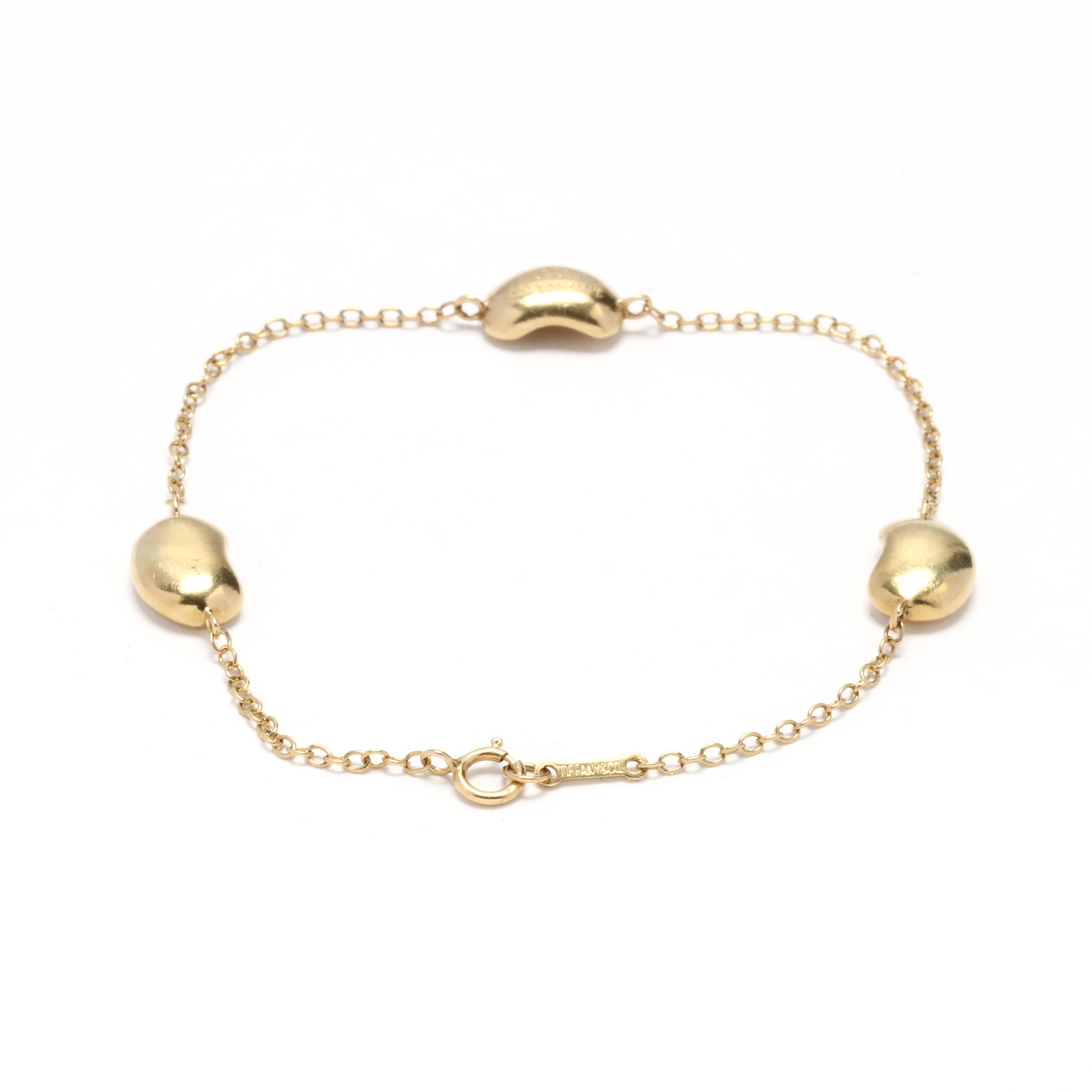 Ein Armband aus 18 Karat Gelbgold mit drei Bohnen, entworfen von Elsa Peretti für Tiffany and Company. Dieses Armband besteht aus einer dünnen Kabelkette mit drei Bohnenmotiv-Charmen und einem Federringverschluss.


Länge: 7 Zoll.

Breite: 7.4