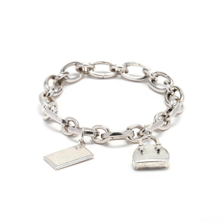 A sterling silver charm bracelet by Tiffany and Company. This bracelet features hidden lobster clap links with a diamond set envelope charm and a purse charm.



Stones:

- diamond, 1 stone

- full cut round

- 1.75 mm

- approximately .02 total