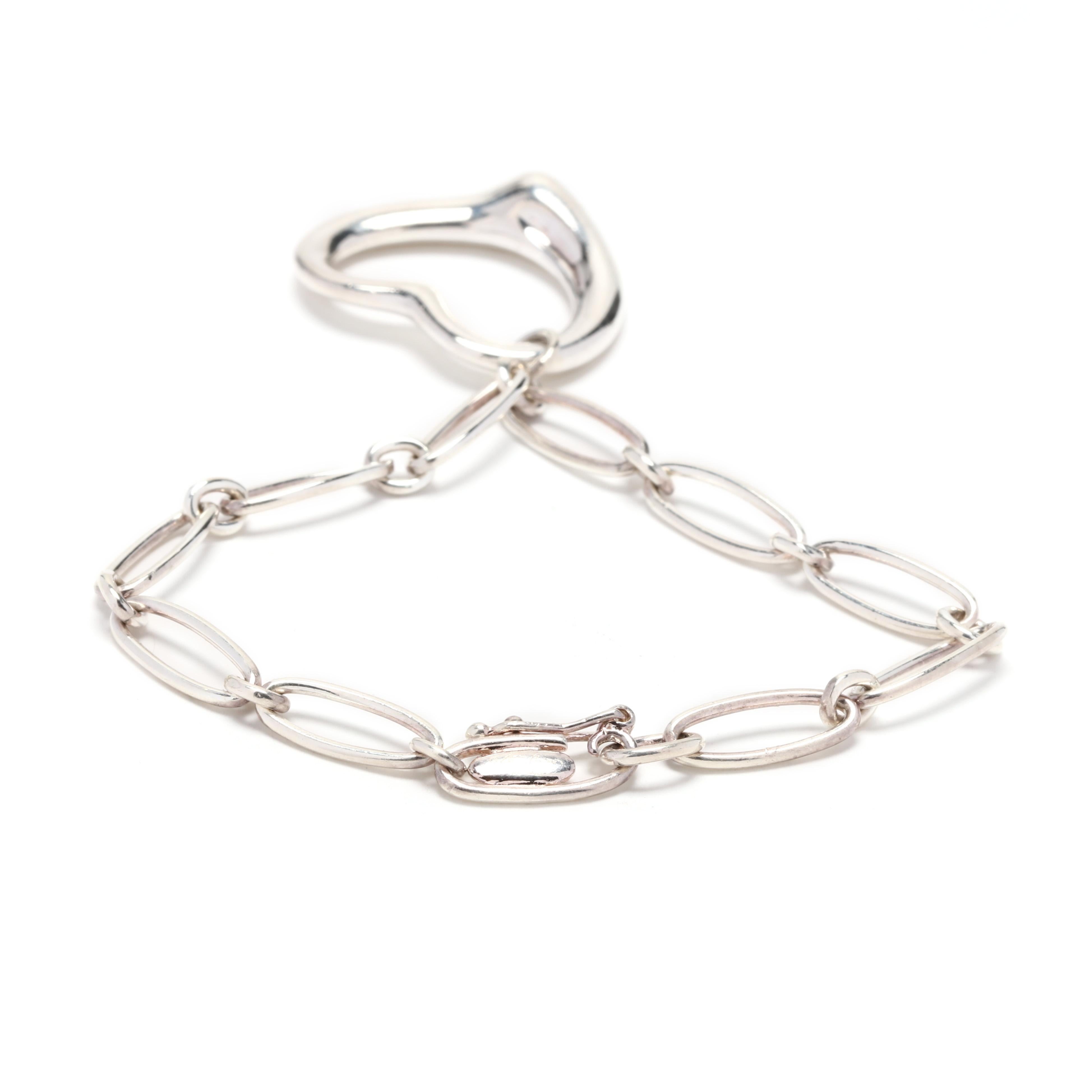 A Tiffany and Company sterling silver open heart charm bracelet. This bracelet features alternating oblong oval and round links with a large tapered open heart charm and a hidden clasp.



Length: 6.5 in.



Width of Bracelet: 5.75 mm



Length of