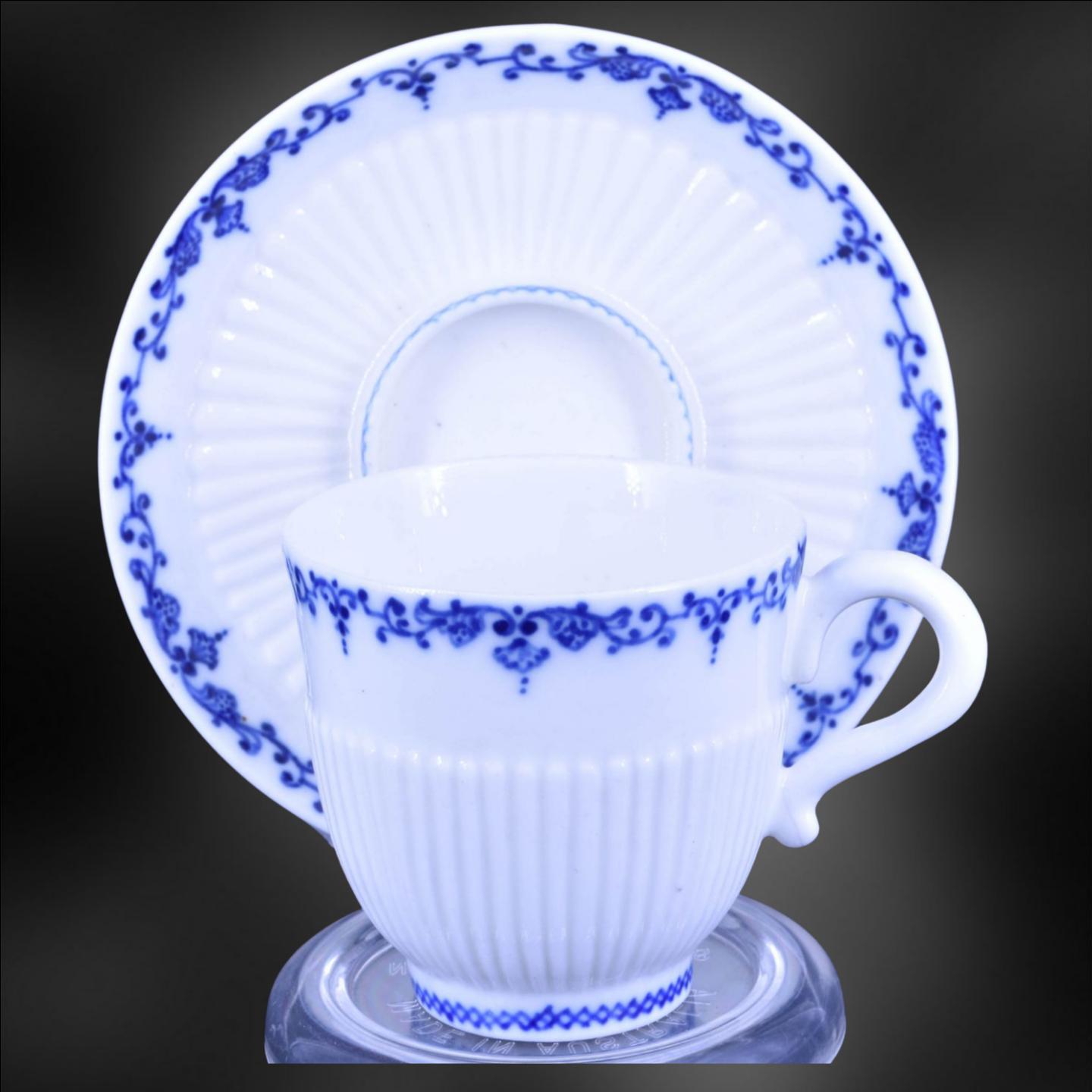 Both cup and saucer with moulded reeding and decorated in underglaze blue with scrolled lambrequin borders.

Saint Cloud porcelain is a type of soft-paste porcelain produced in the French town of Saint Cloud from the late 17th century to the