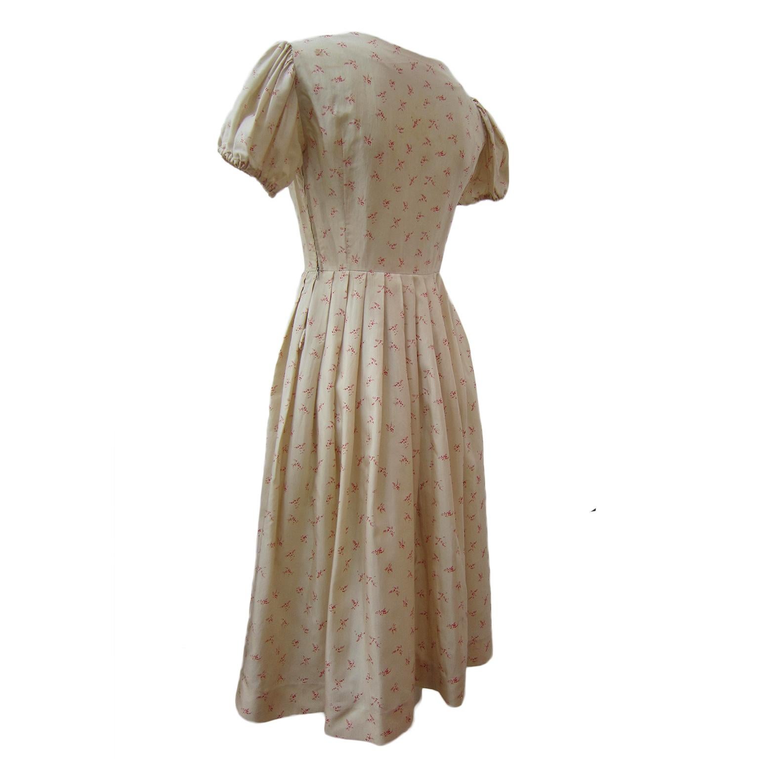 Hübsches kurzes Kleid mit Puffärmeln aus den 1950er Jahren. Das Material mit beigefarbenem Grundton hat einen fast teeähnlichen Effekt und ist durchgehend mit roten Blumen bedruckt. Tailliert geschnittenes Mieder mit Schleifen am Ausschnitt. Schicke