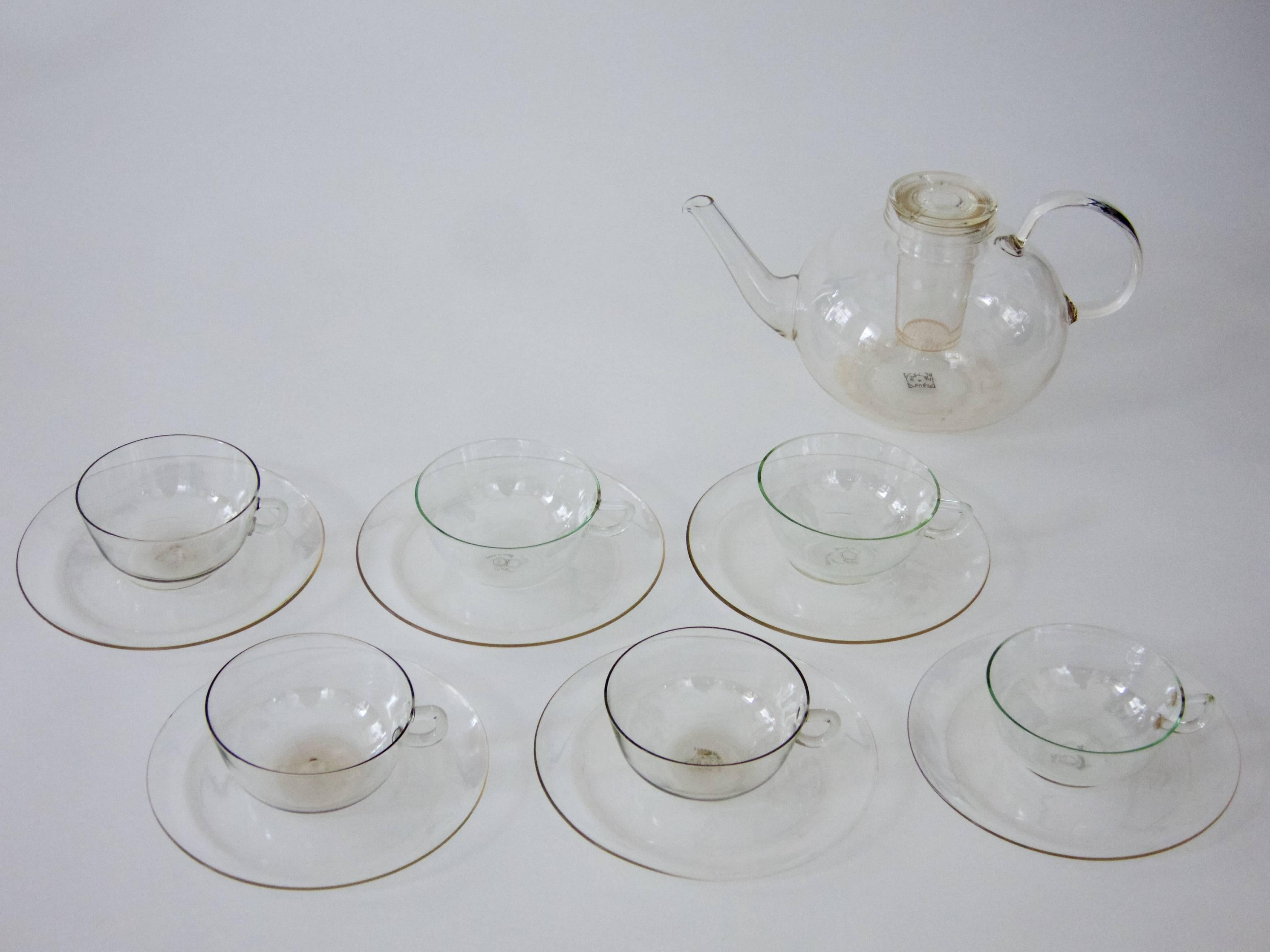 Tea set, circa 1925
comprising a teapot with internal glass filter and a lid. furthermore six cups with plates.

fire-proof, clear borosilicate glass

all cups and plates marked with: Jenaer Glas, a circle in a Pentagon and Teho
teapot marked with a