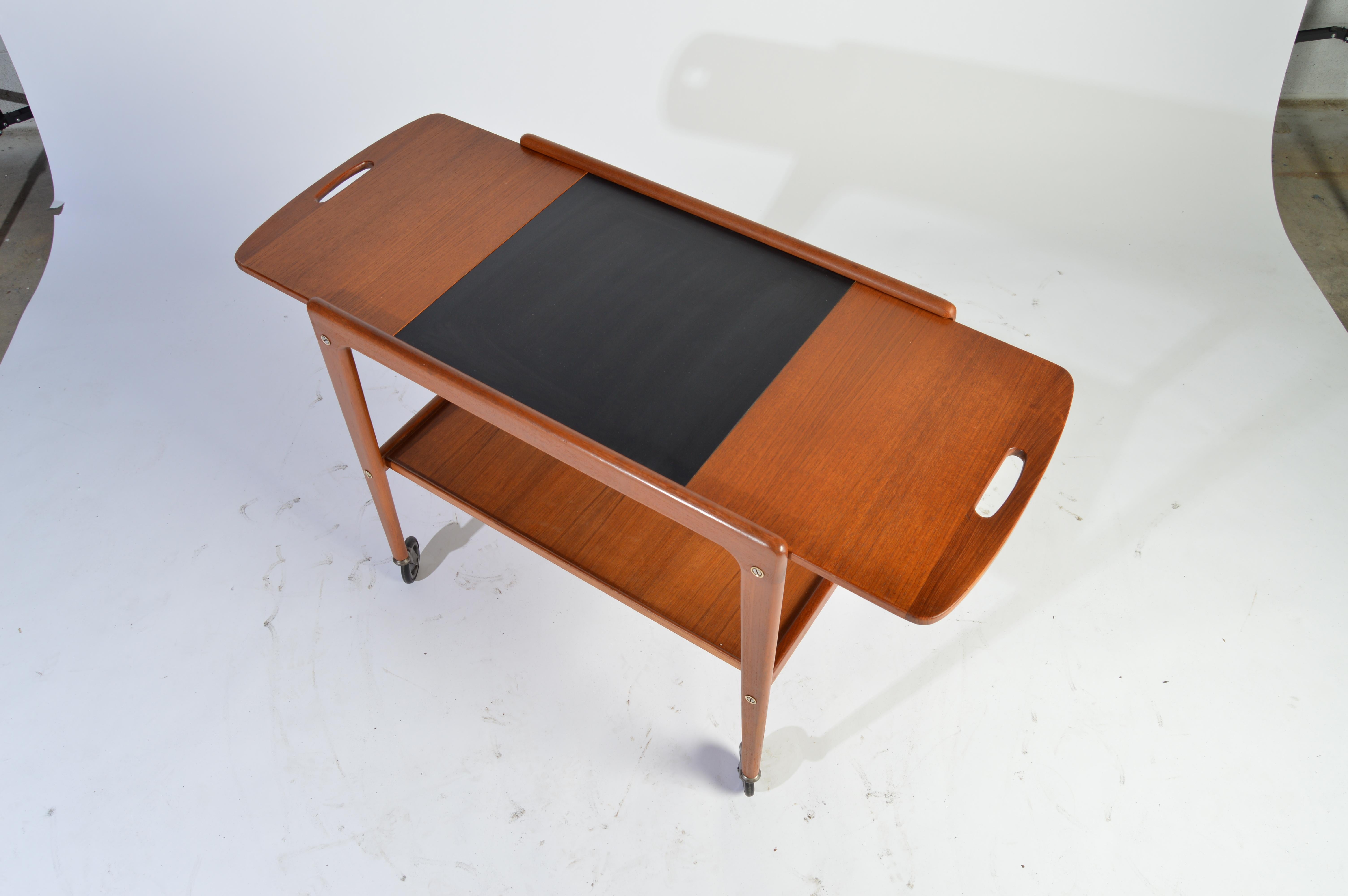 Adjustable tea trolley having teak frame with black laminate top designed by Yngve Ekstrom, Sweden, 1956.
Expanded width is 39.5